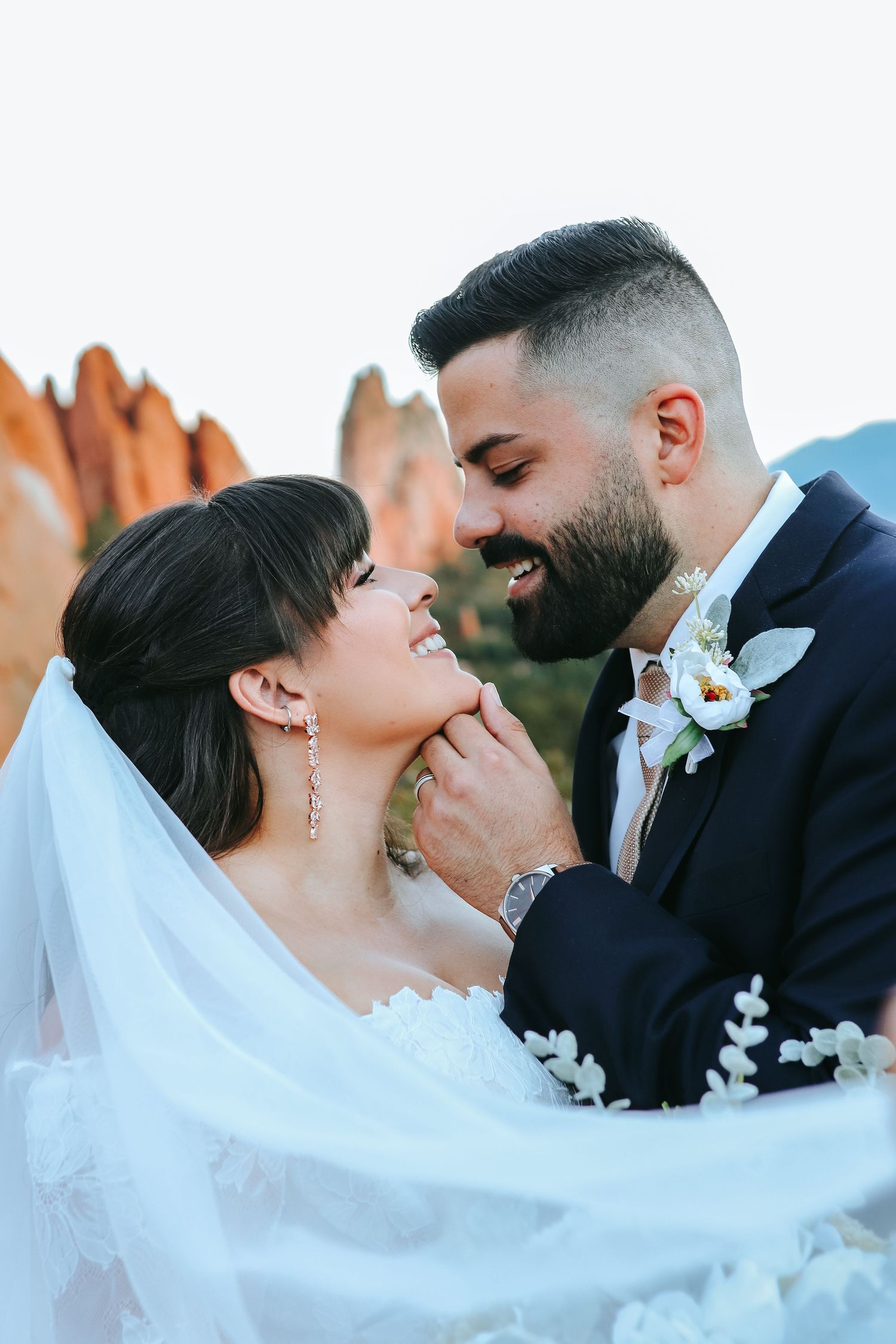 Smiling bride and bearded groom sharing a romantic moment with veil flowing in wind.