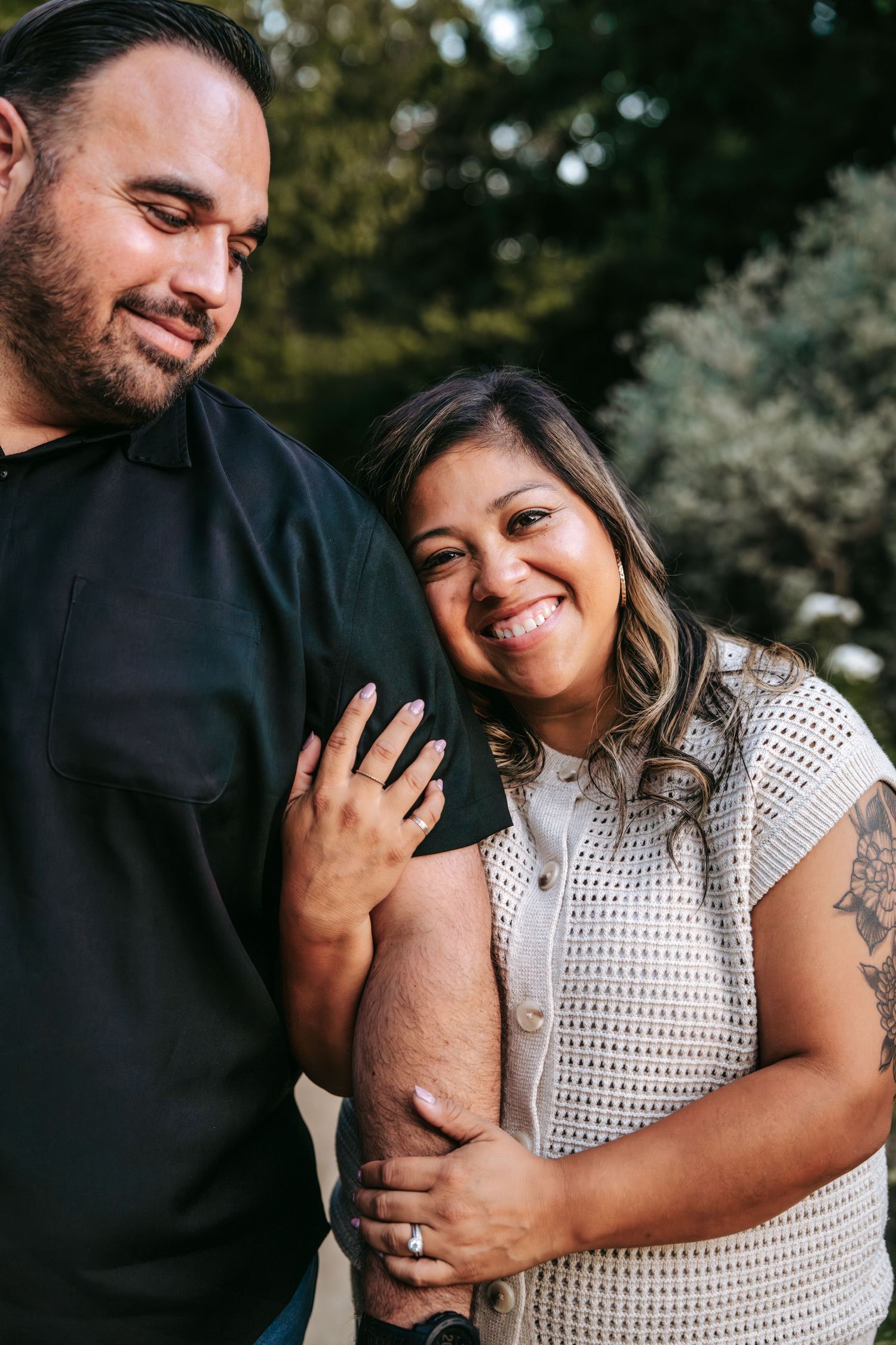 Loving couple smiling and embracing closely in a sunlit outdoor park setting.