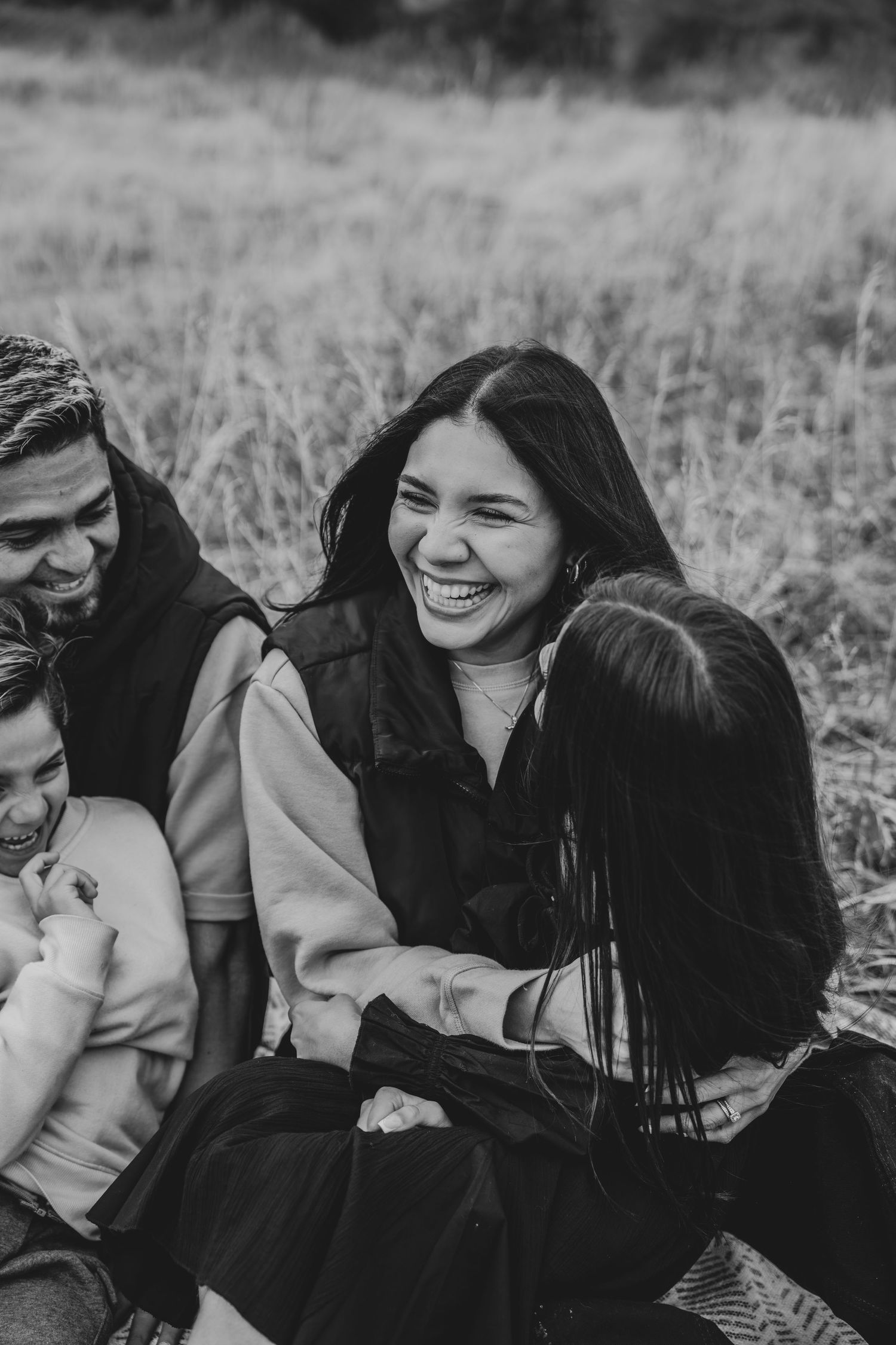 Black and white photo of joyful family laughing together in an autumn field.