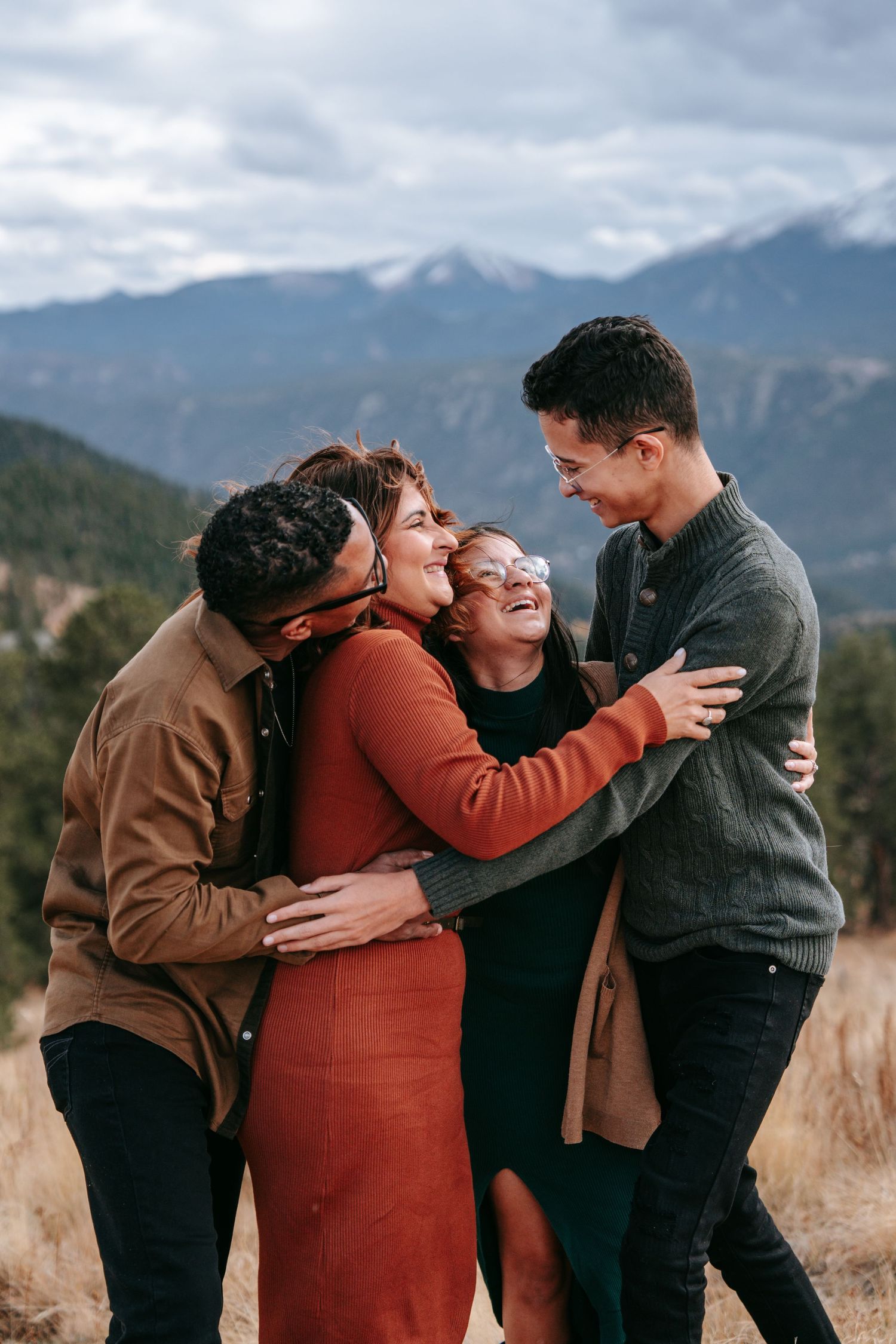 Family of four embracing and laughing together in a mountain meadow during an autumn outdoor photo session.