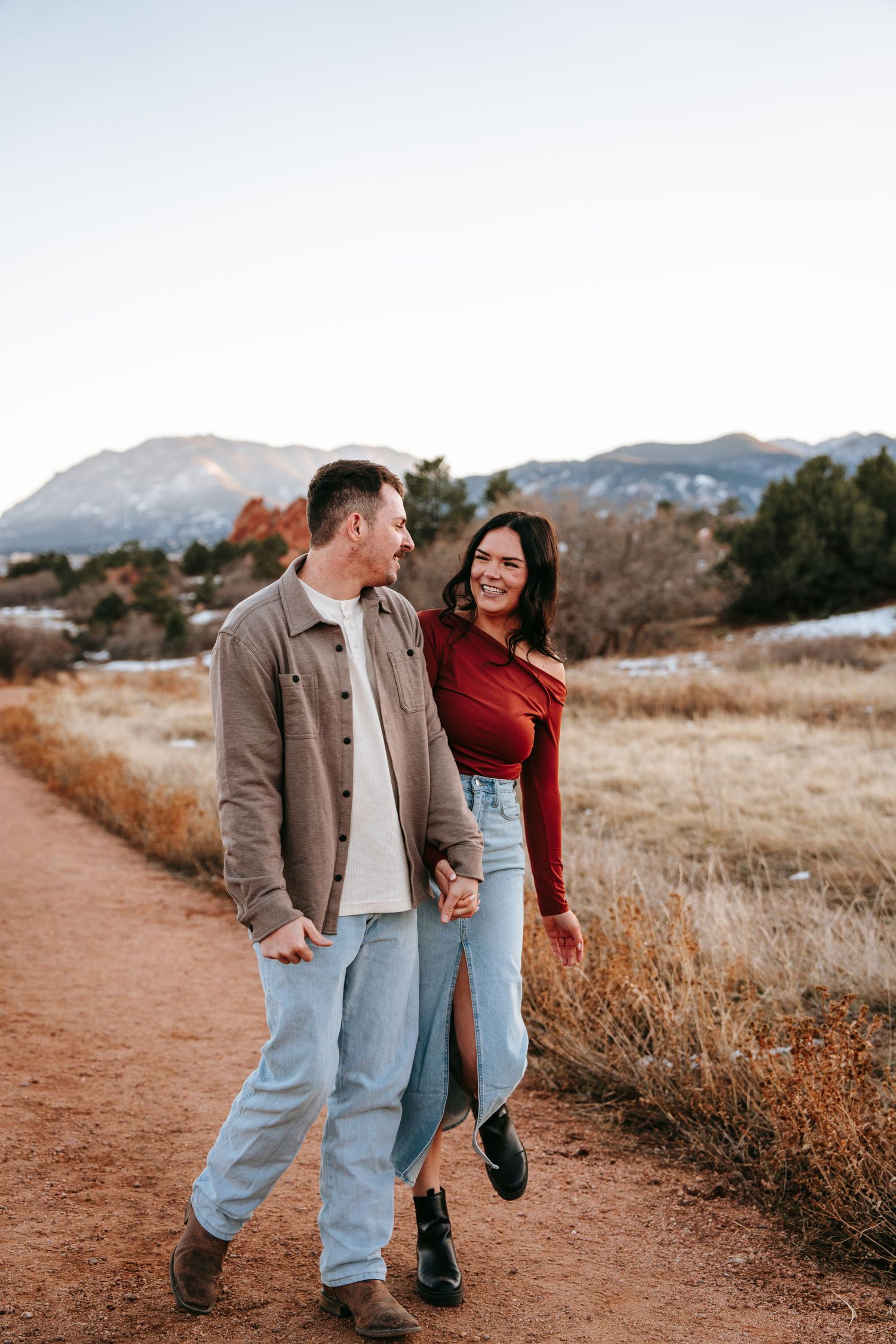 Couple smiling and holding hands while strolling on a scenic red dirt mountain trail.