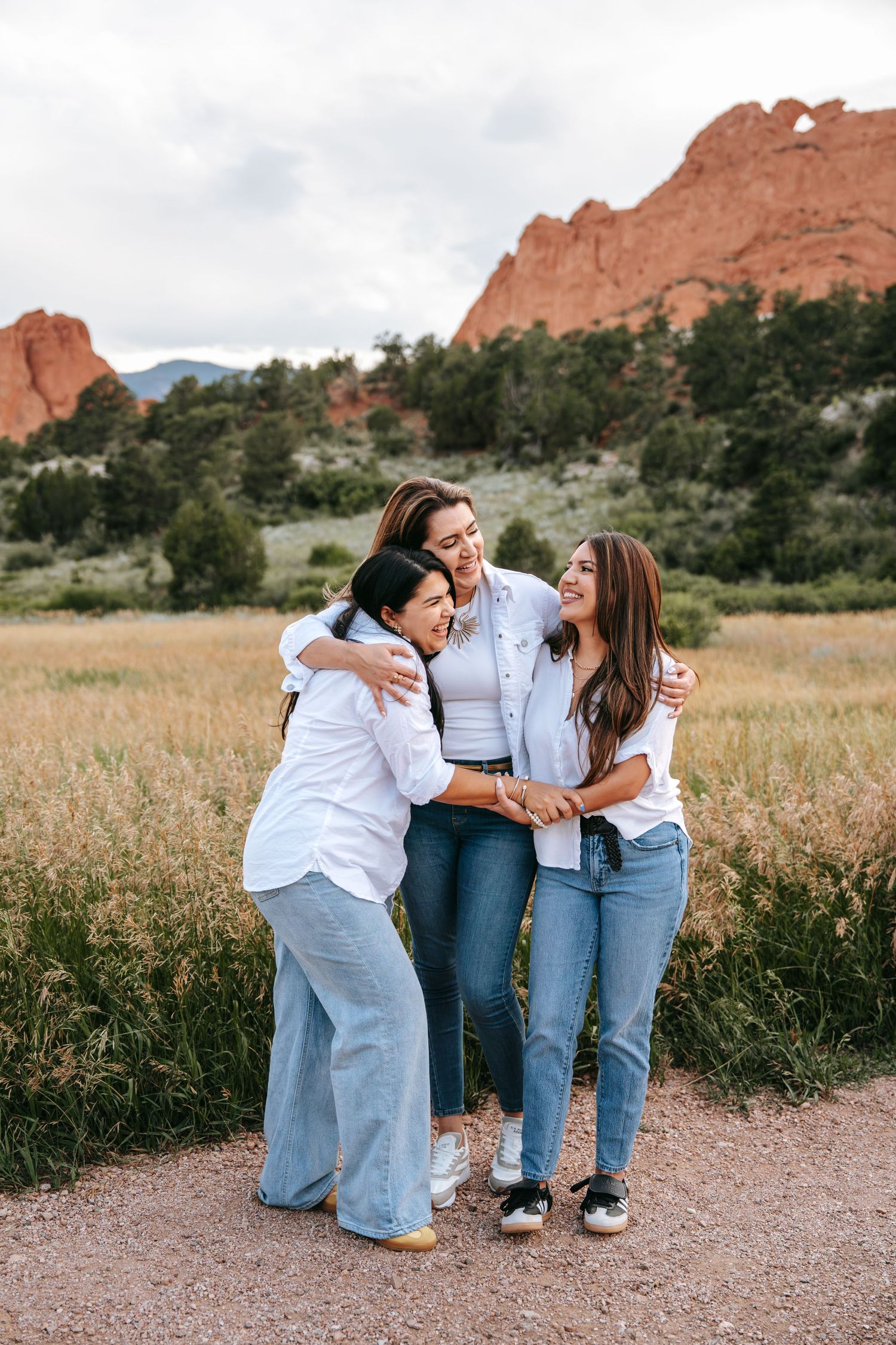 Three women laughing and hugging each other on a path with stunning red rock formations in the background.