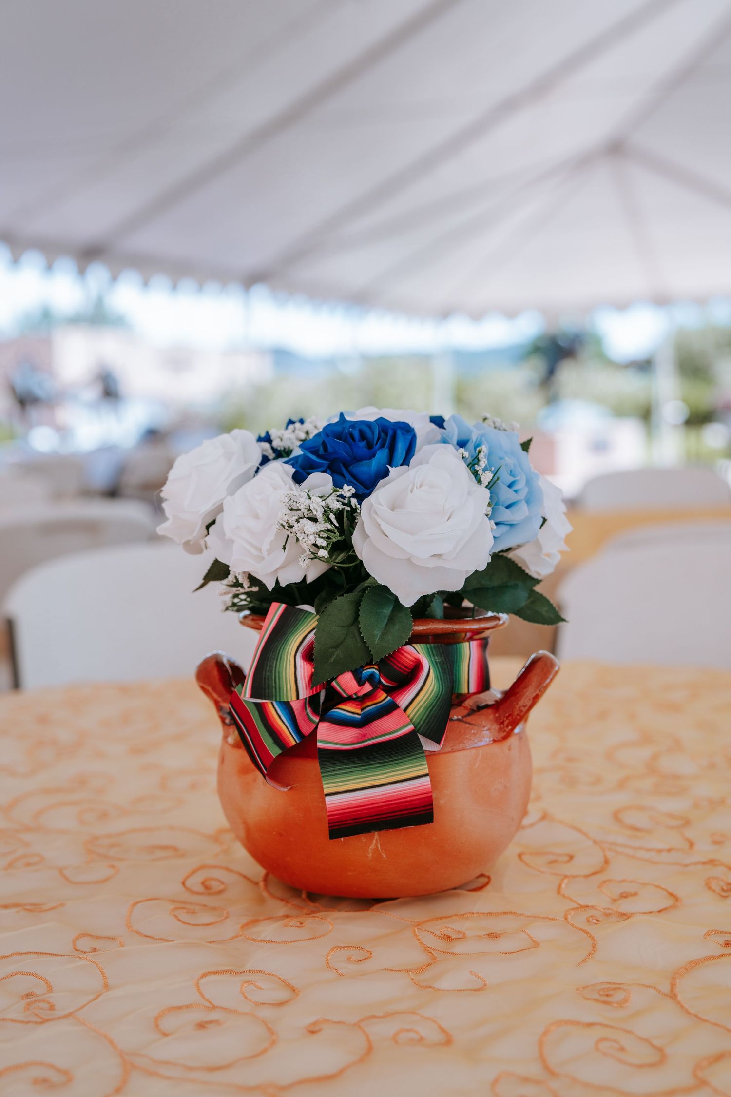 Blue and white rose floral centerpiece in a copper teapot with a serape ribbon bow.
