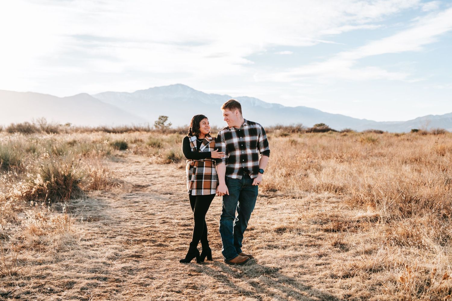 Couple in matching plaid shirts walking together in a dry field with mountains in the background.