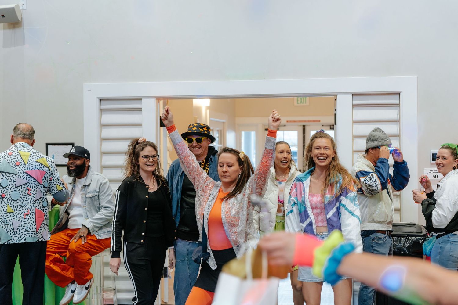 Excited group of people celebrating indoors, raising hands in joy at a colorful festive event.