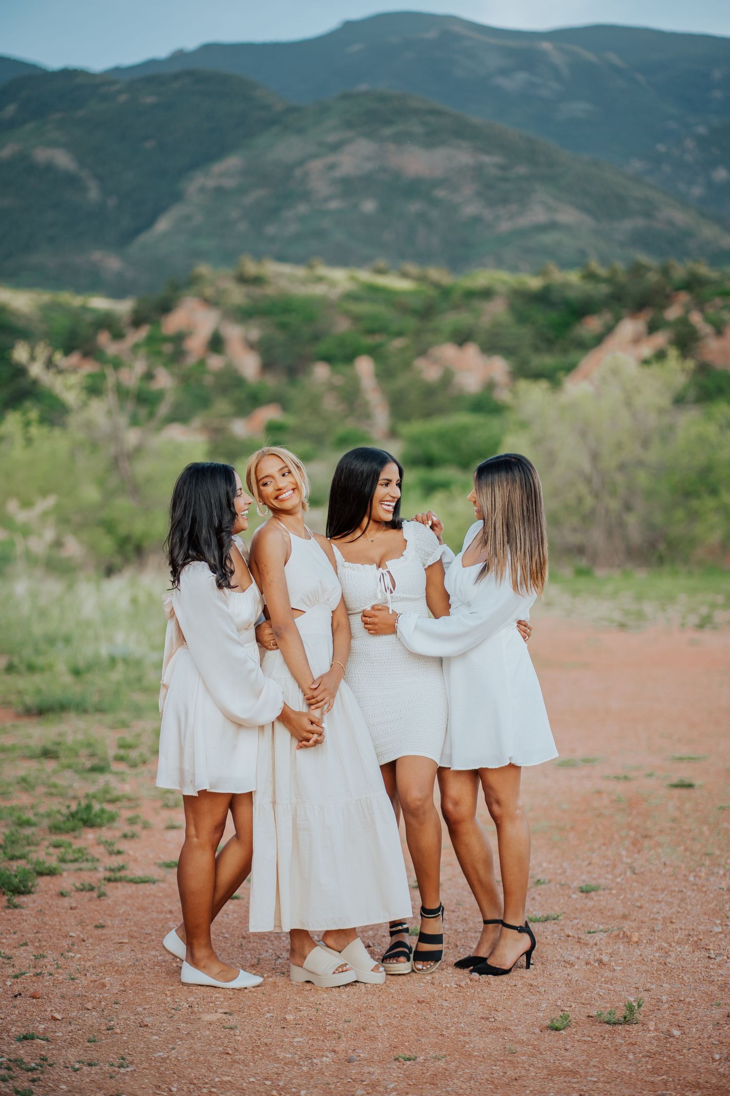 Four women in white dresses pose together at a scenic red rock location in Colorado.