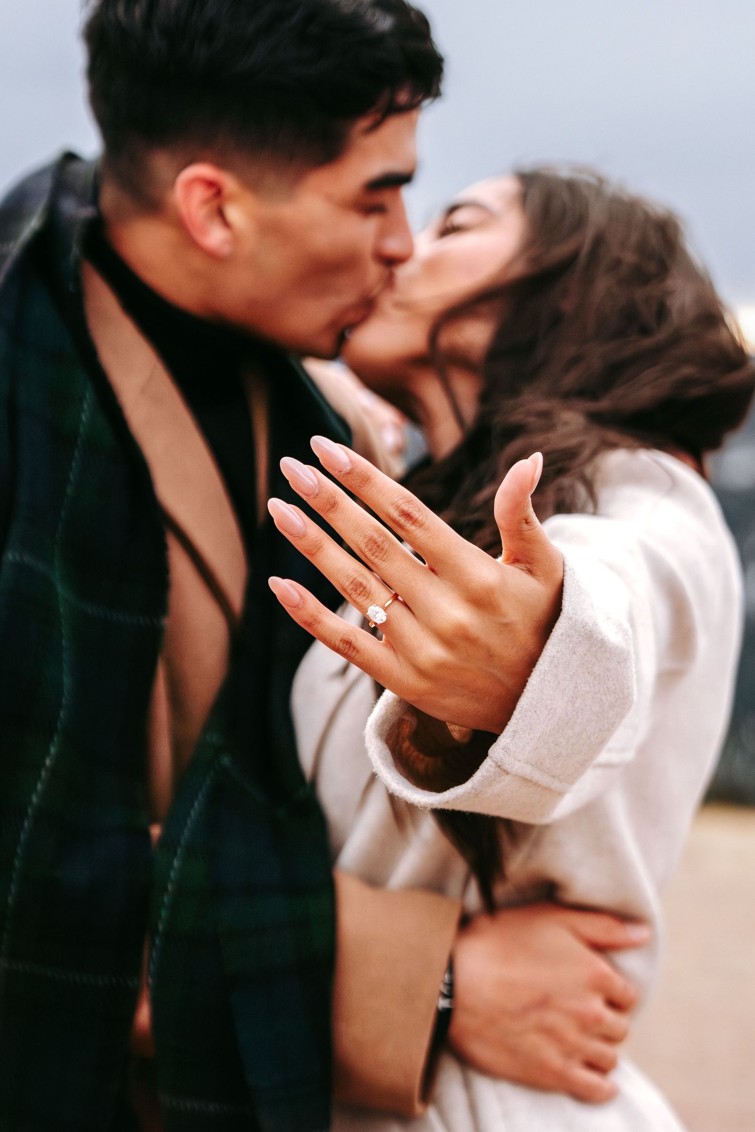 Engaged couple kissing while woman displays diamond engagement ring toward camera.