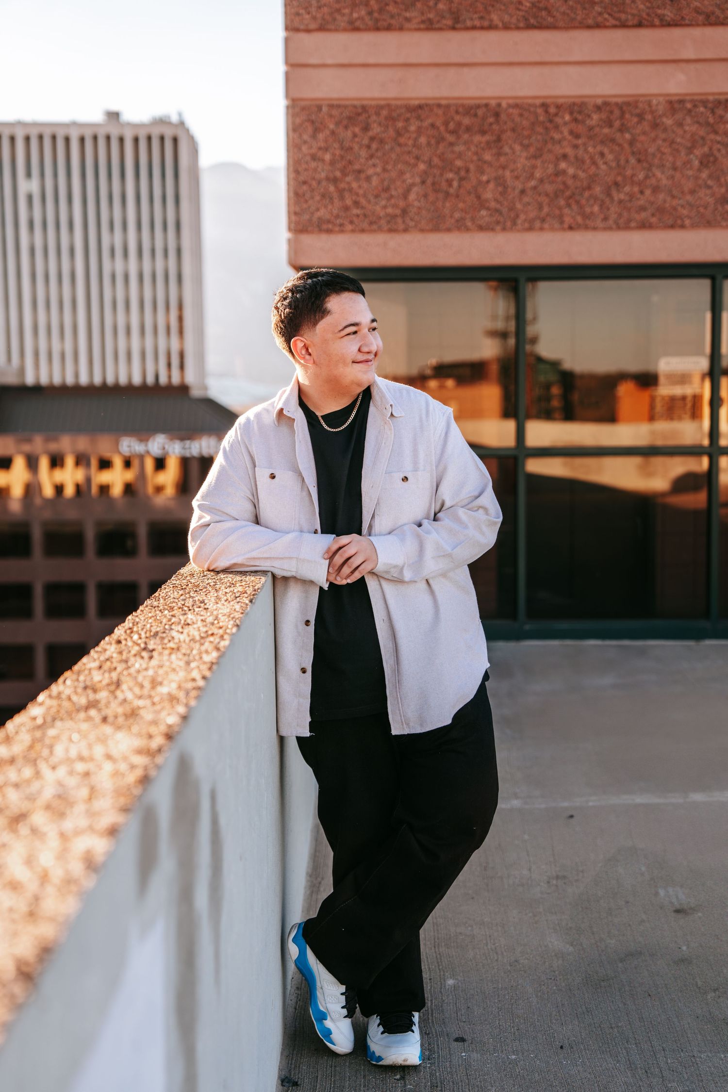 Young man in white shirt leaning on rooftop ledge at golden hour in city.