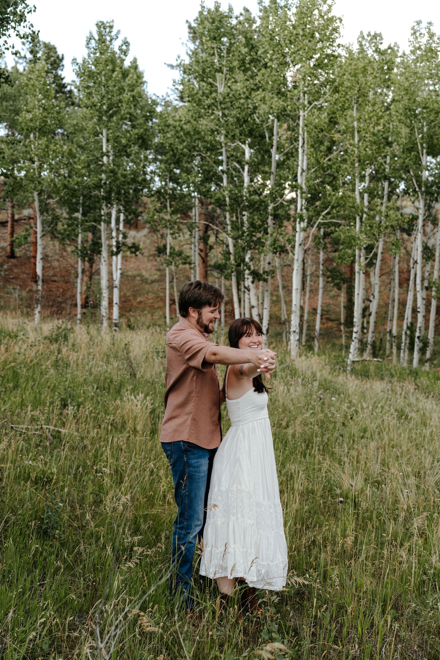 Couple dancing in a meadow with white birch trees, man in brown shirt embracing woman in white dress.