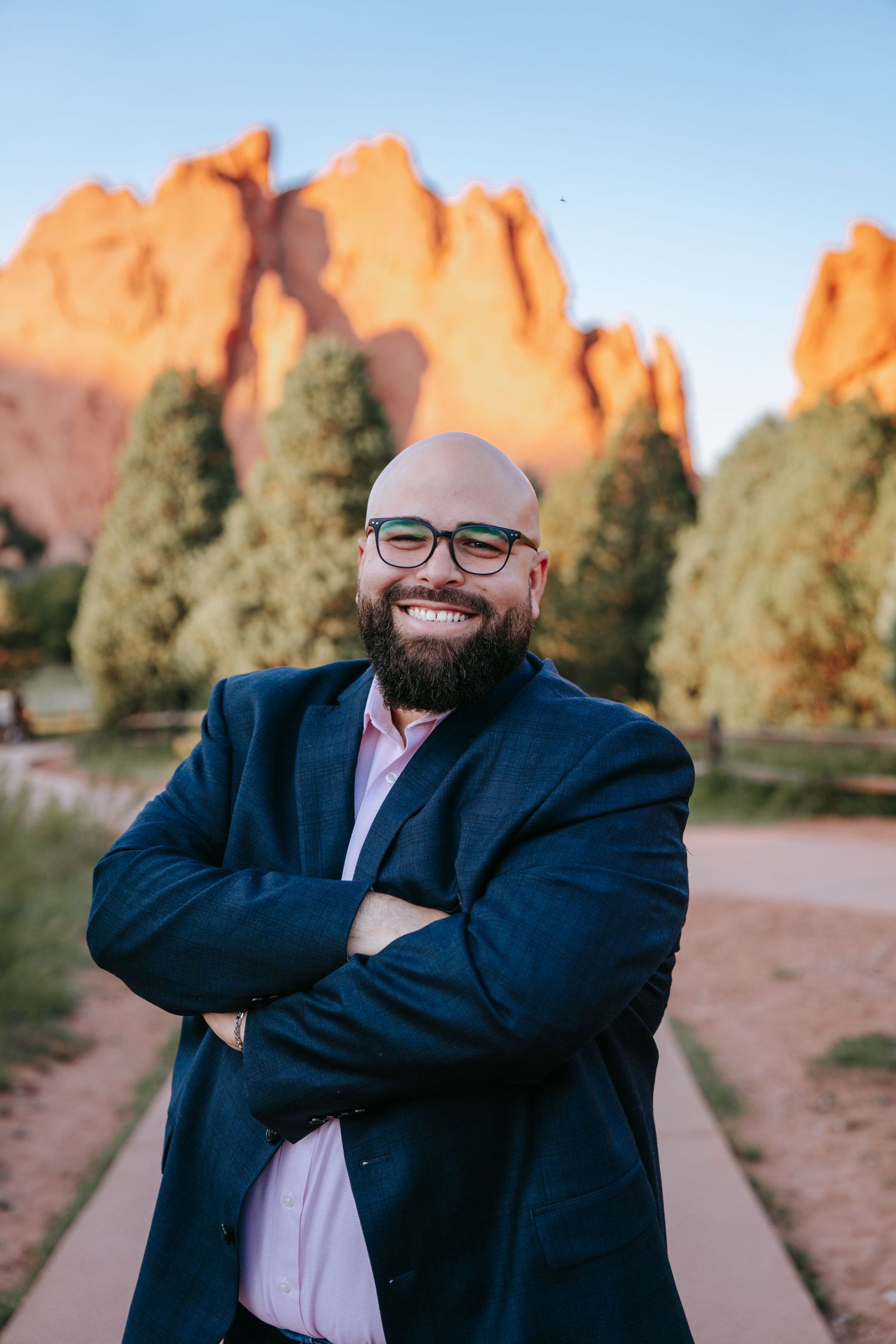 Confident bald bearded man in navy blazer with arms crossed at Garden of the Gods.