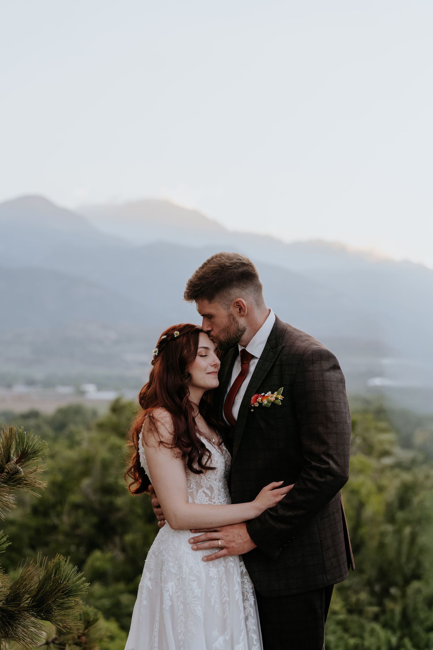 Bride and groom embracing at sunset with a stunning mountain landscape backdrop during their wedding portraits.