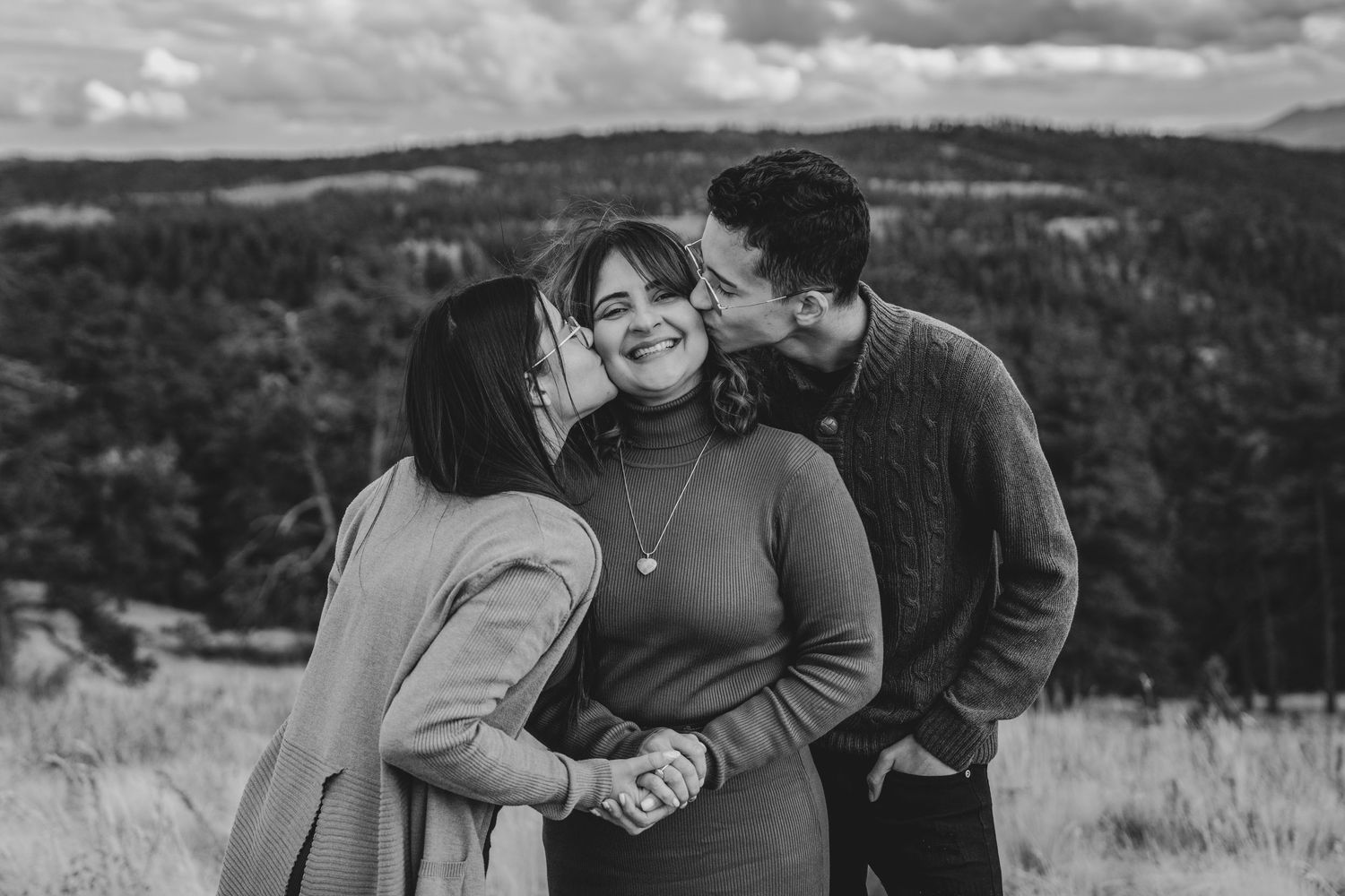 Black and white photo of a woman being kissed on both cheeks by two people in a mountain setting.
