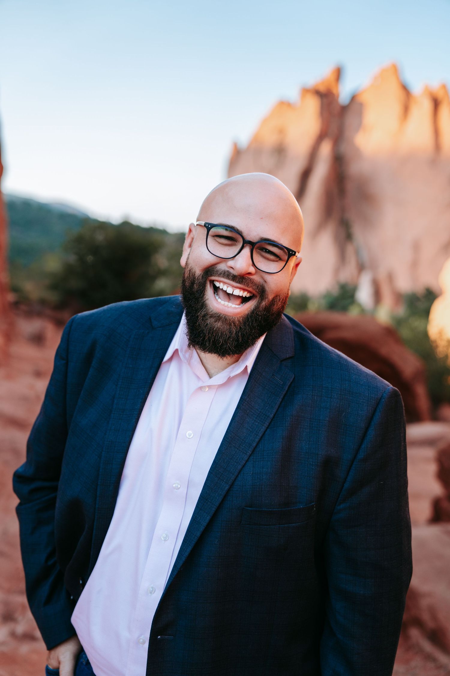 Joyful bald bearded man in navy blazer laughing at Garden of the Gods at sunset.