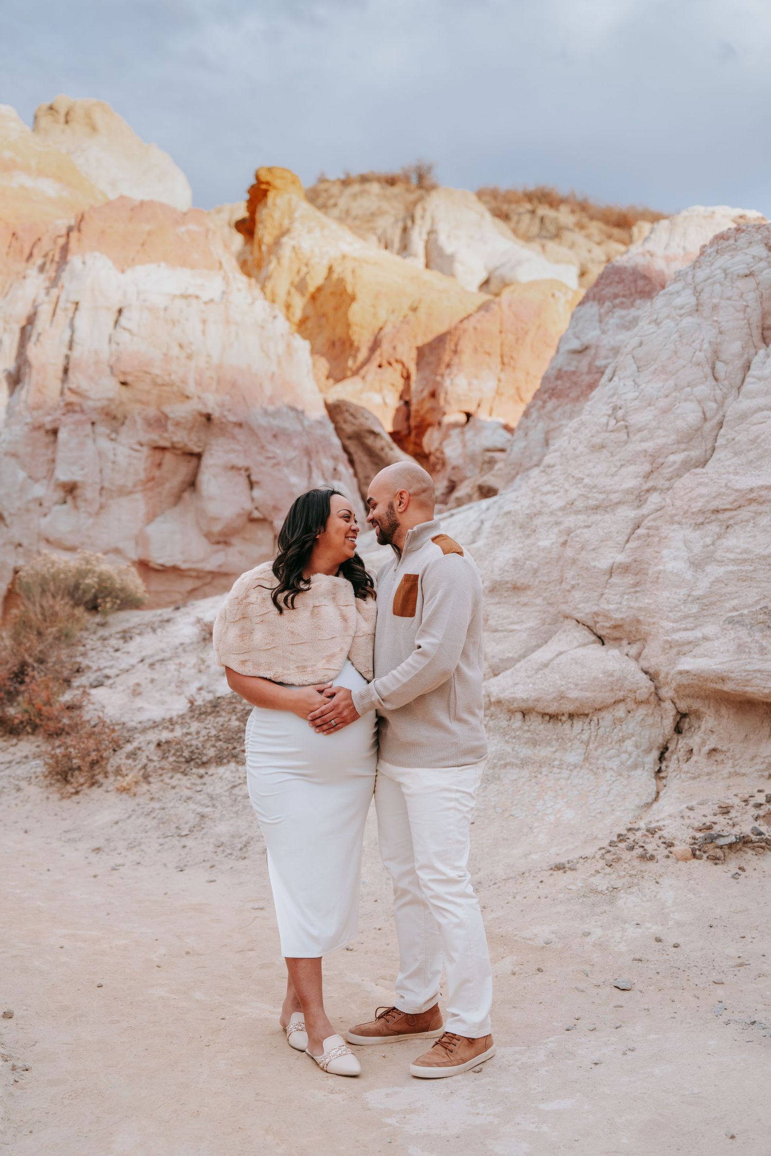 Expecting couple gazing at each other lovingly in front of vibrant painted desert rock formations.