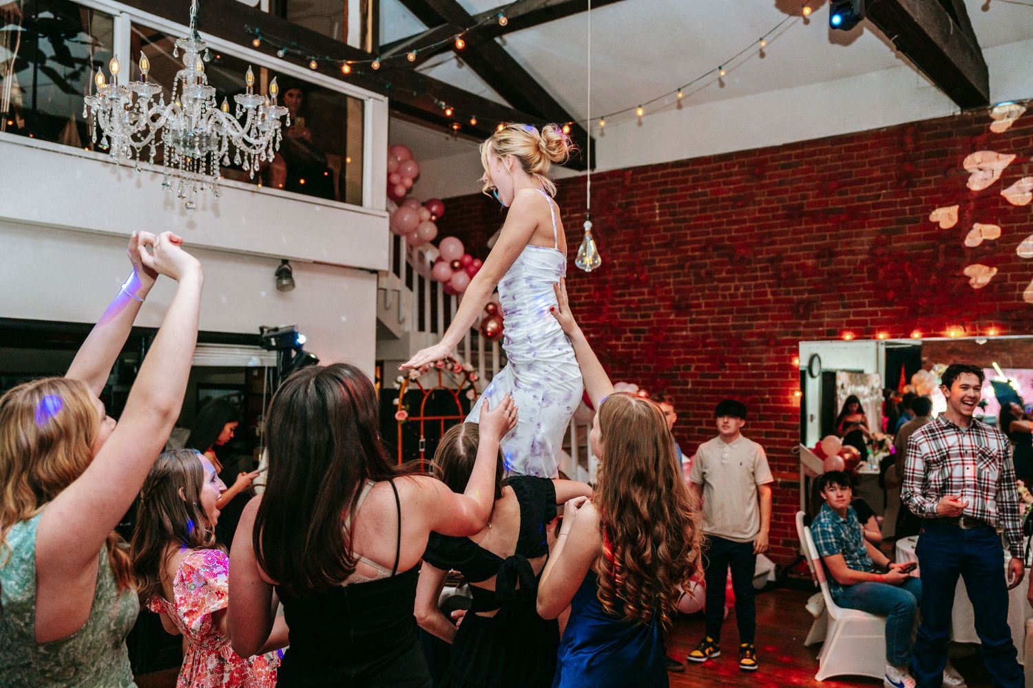 Guest lifted by crowd on dance floor during lively quinceañera celebration in rustic venue.