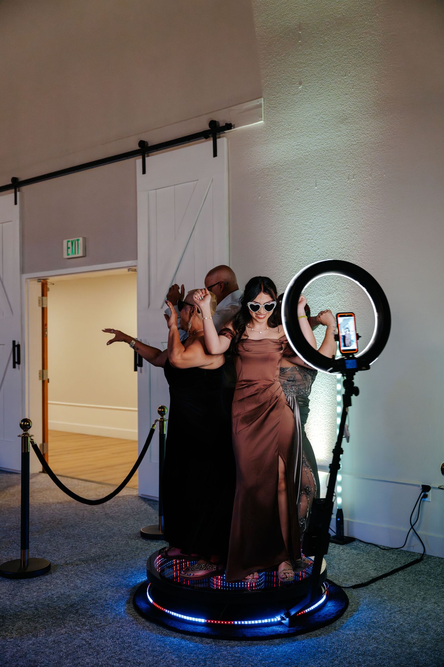 Three people posing at a photo booth with a ring light and smartphone at an elegant indoor event venue.