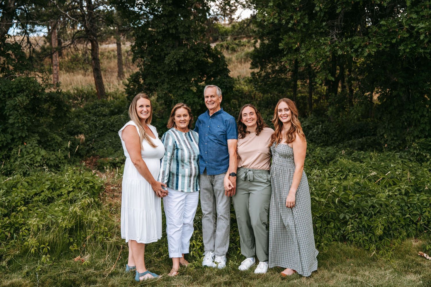 Family of five smiling together outdoors in a lush green setting for a portrait photo.