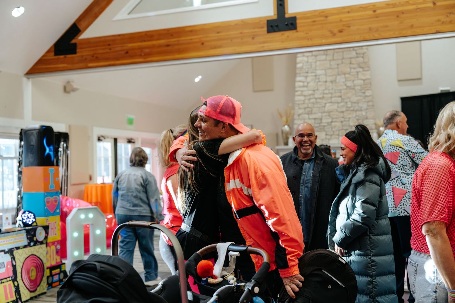 People hugging and socializing at a festive indoor community gathering with colorful decorations.