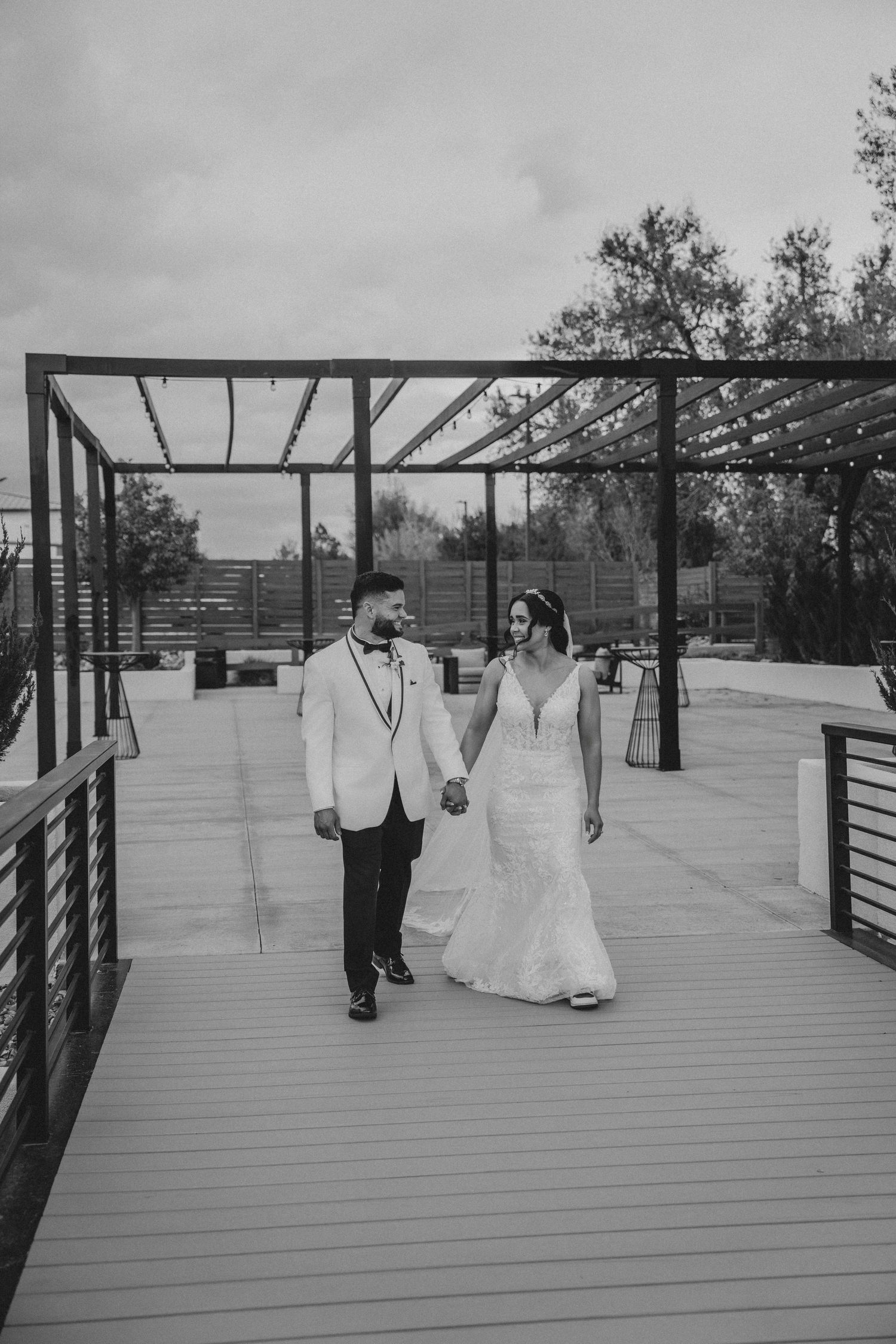 Black and white photo of a bride and groom holding hands on a wooden deck at their outdoor wedding venue.