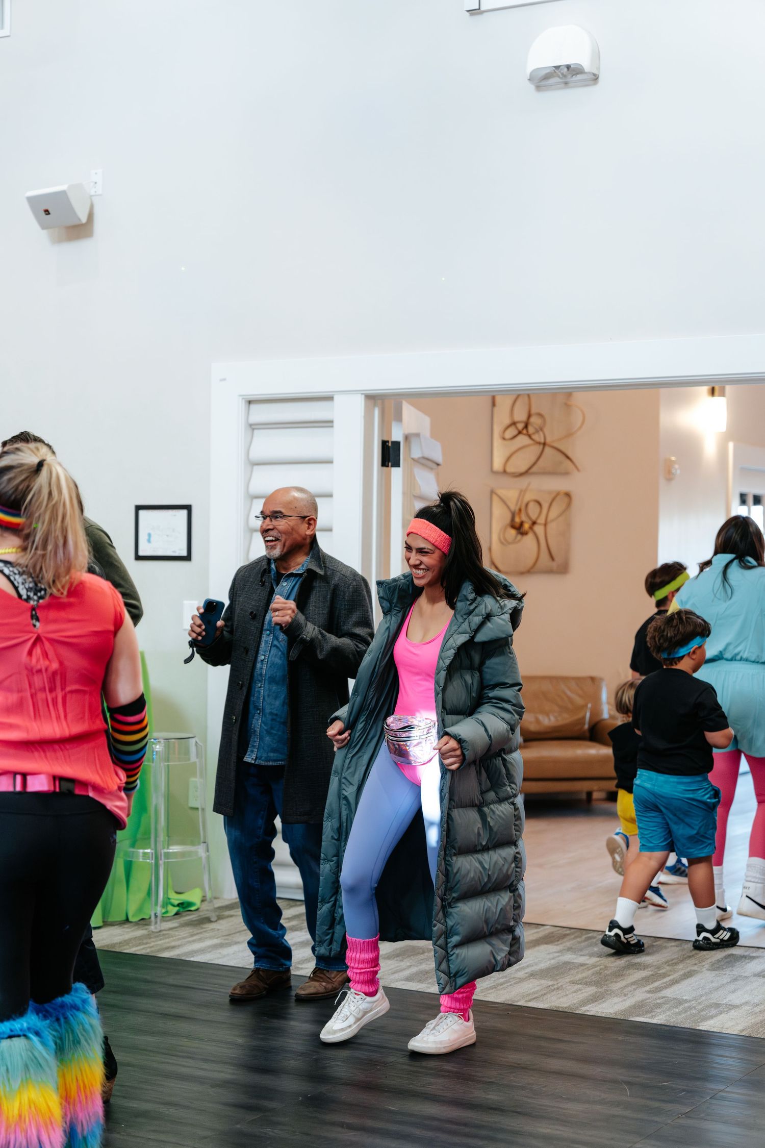 Group of people in colorful 80s-themed workout attire socializing indoors at a retro fitness event.