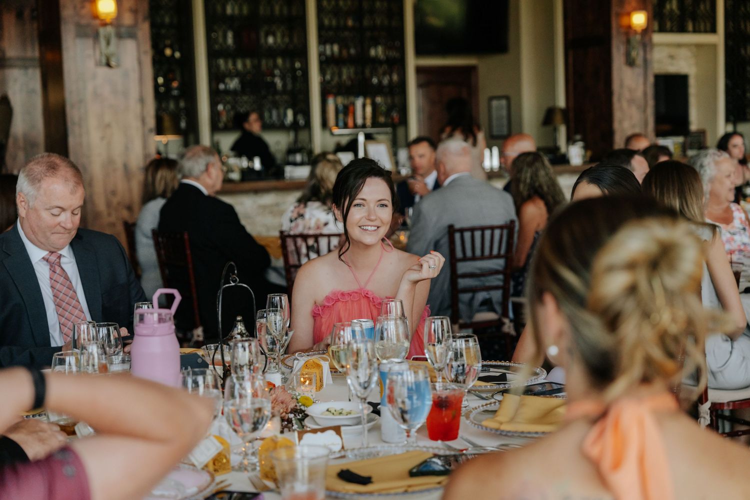 Smiling wedding guest in a pink dress seated at an elegantly set reception dinner table.
