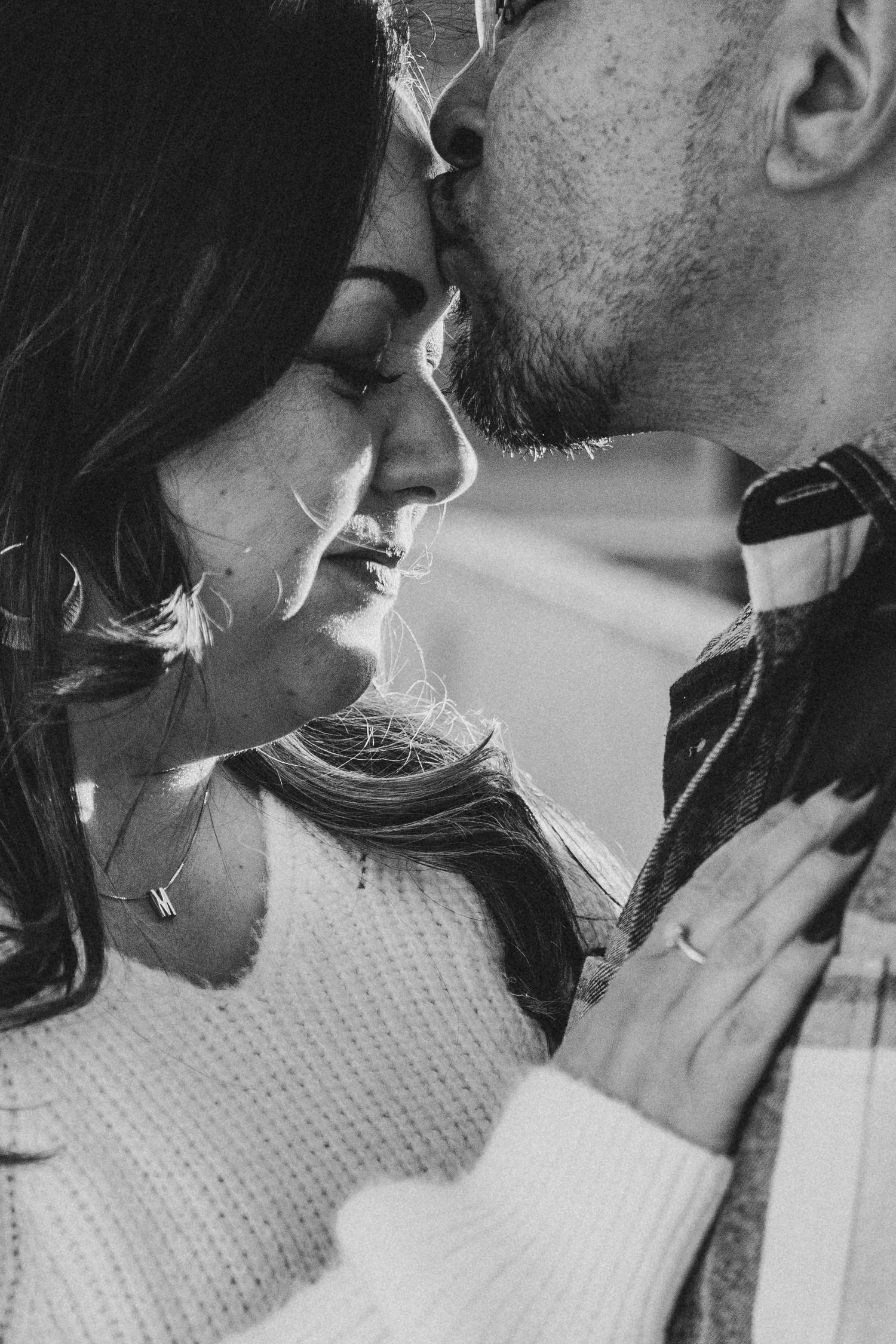 Black and white close-up of a couple sharing an intimate moment, man kissing womans forehead tenderly.