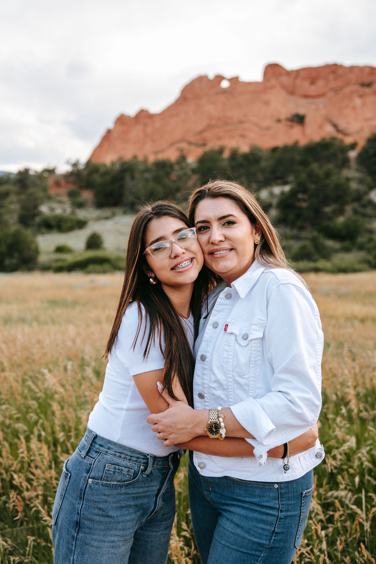 Two women smiling and embracing in a golden field with iconic red rock formations visible behind them.