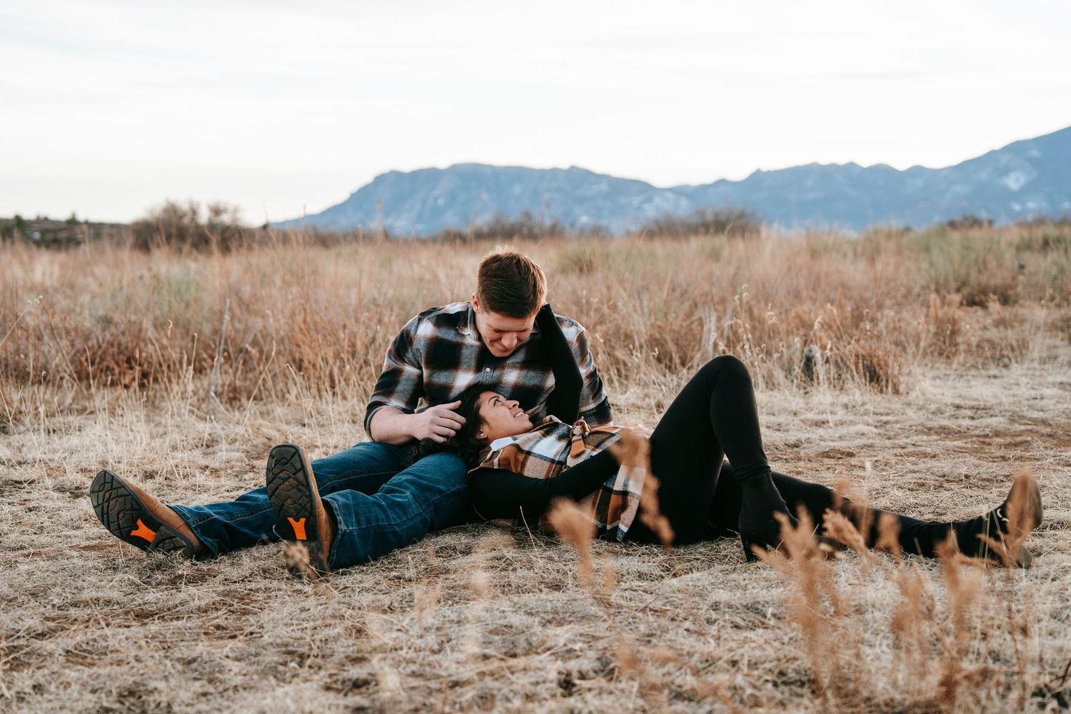Man sitting in dry field reading a book to his dog during an outdoor autumn photoshoot.