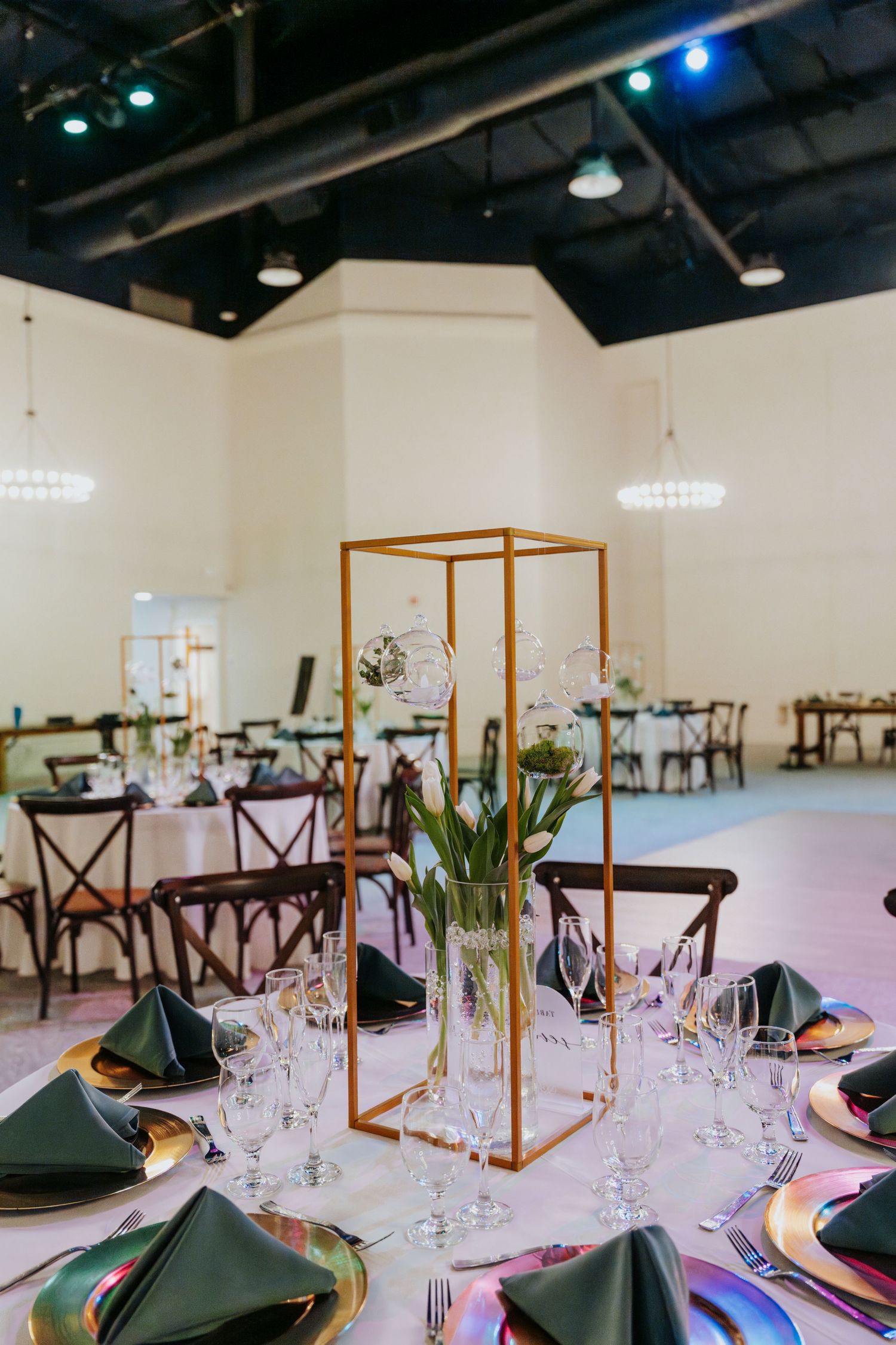 Elegant wedding reception table with gold geometric centerpiece, green napkins, crystal glasses, and iridescent charger plates.