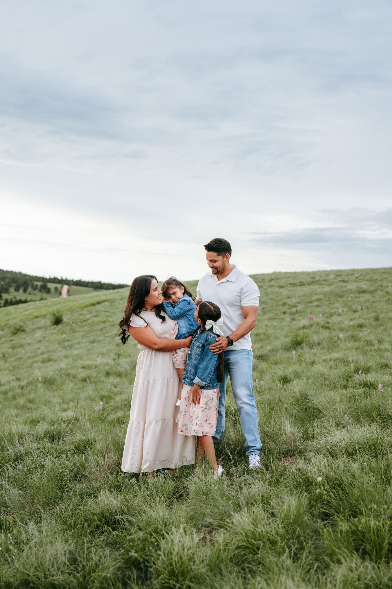 Happy family of three standing together in a green meadow with overcast sky background.