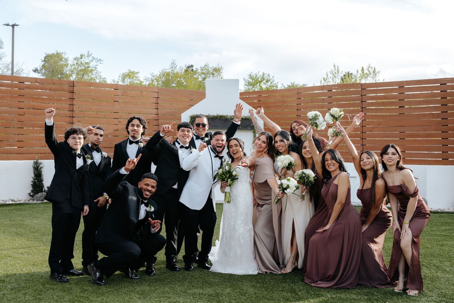 Wedding party celebrating outdoors, bride and groom surrounded by groomsmen in tuxedos and bridesmaids in mauve gowns.