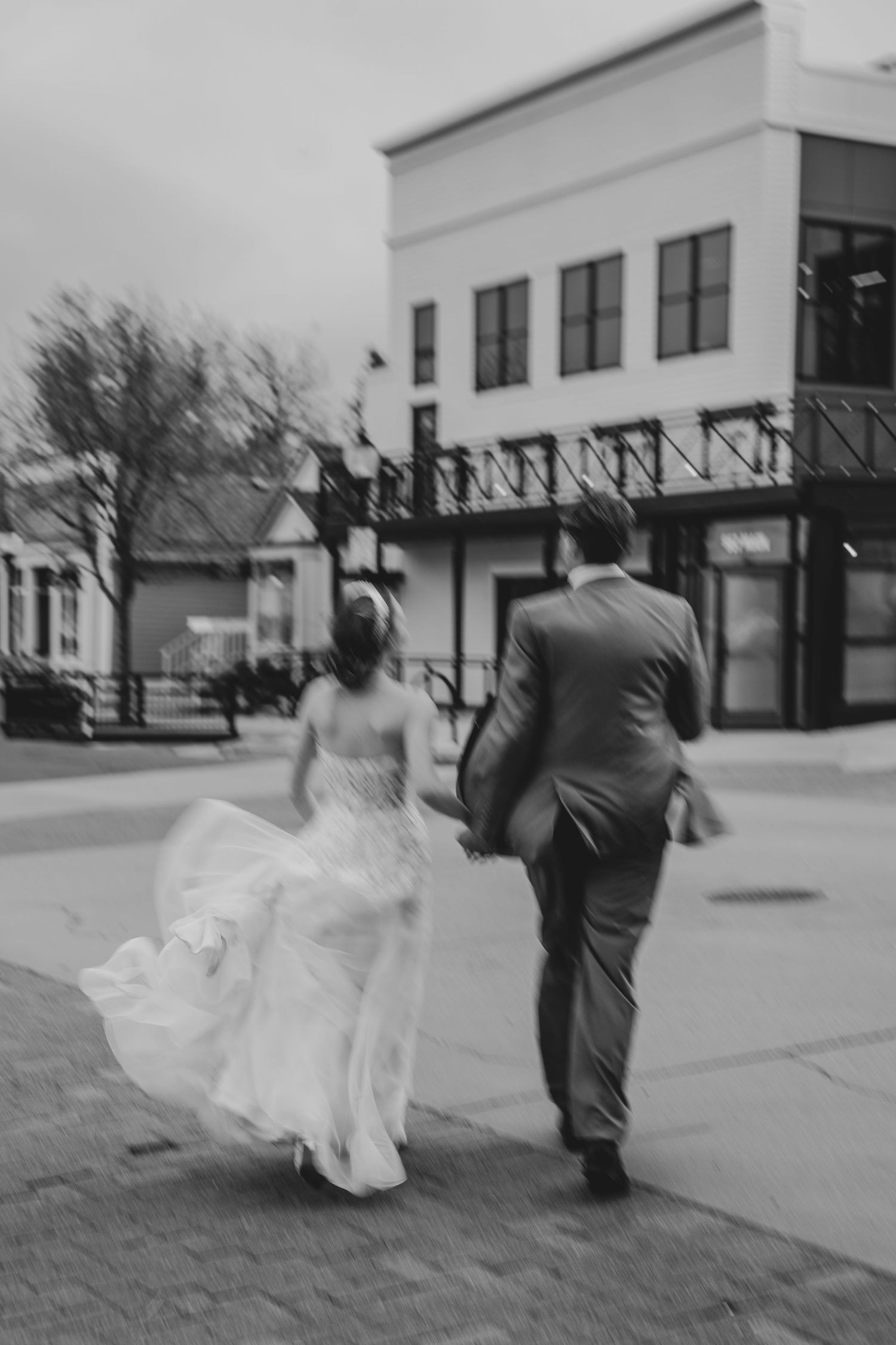 Blurred black and white photo of a bride and groom walking together on a city sidewalk after their wedding.