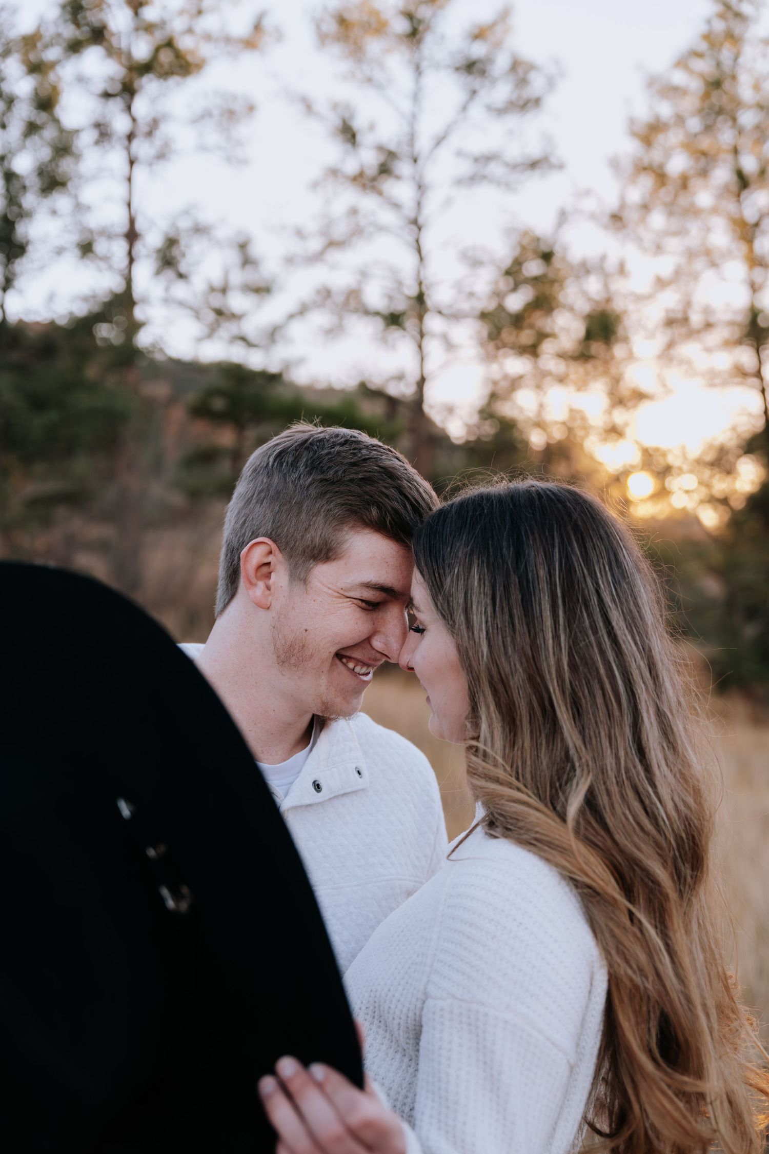 Couple smiling and touching foreheads in a tender romantic moment during golden hour outdoors.