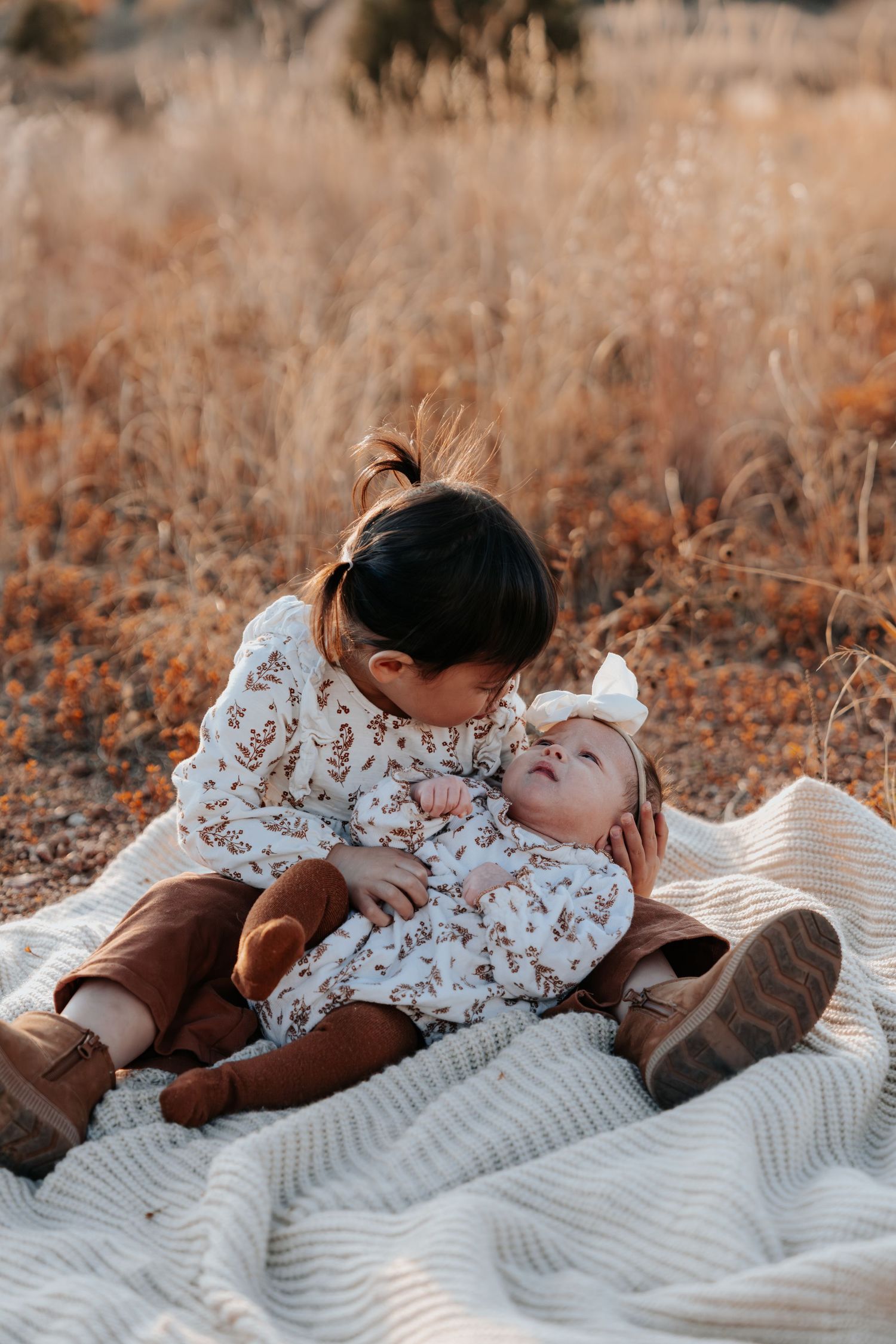Two young siblings sharing a sweet moment on a blanket in a dry autumn field.