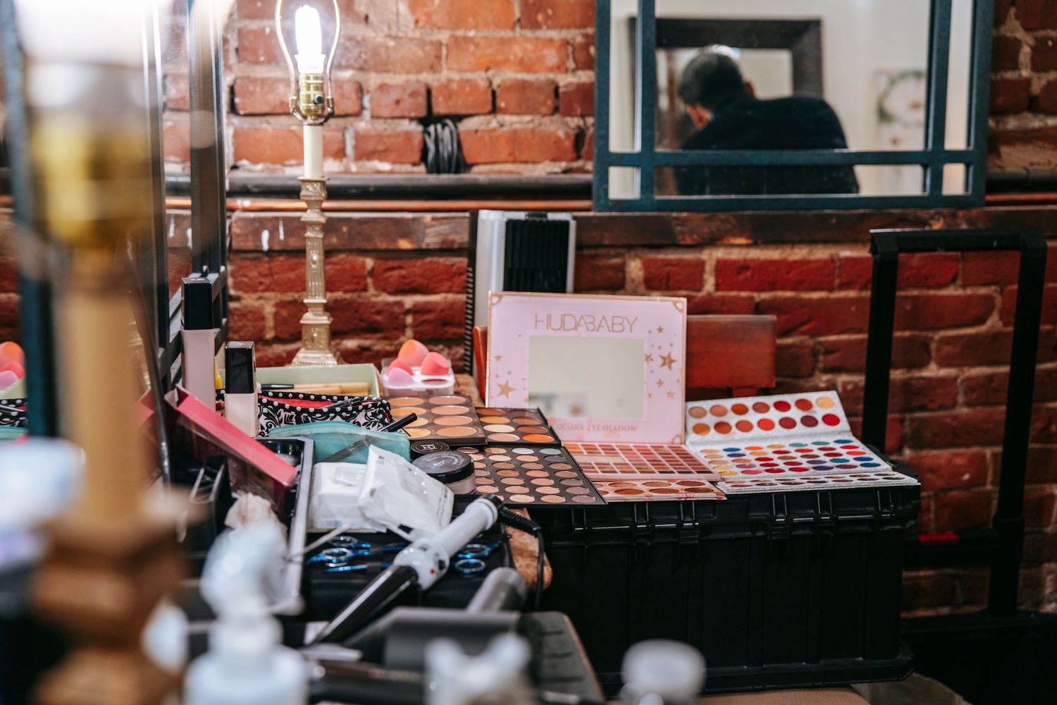 Colorful makeup palette and beauty products arranged on a vanity table with brick wall backdrop at a quinceañera.