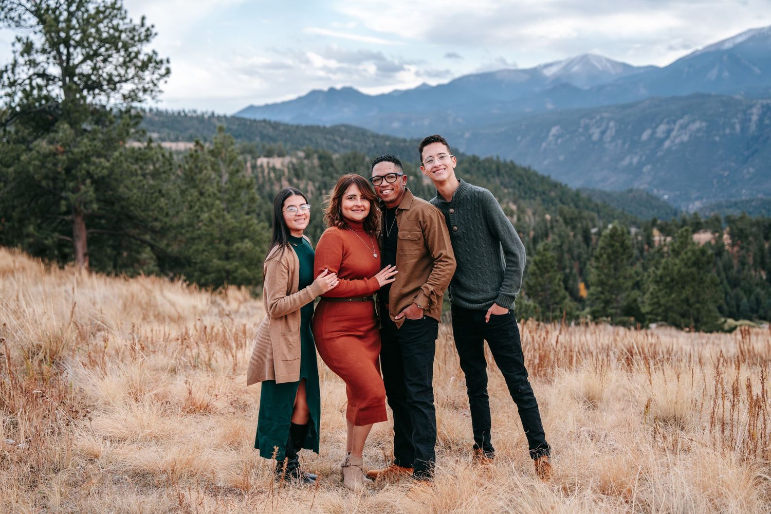 Family of four smiling together in a golden meadow with Rocky Mountain backdrop.