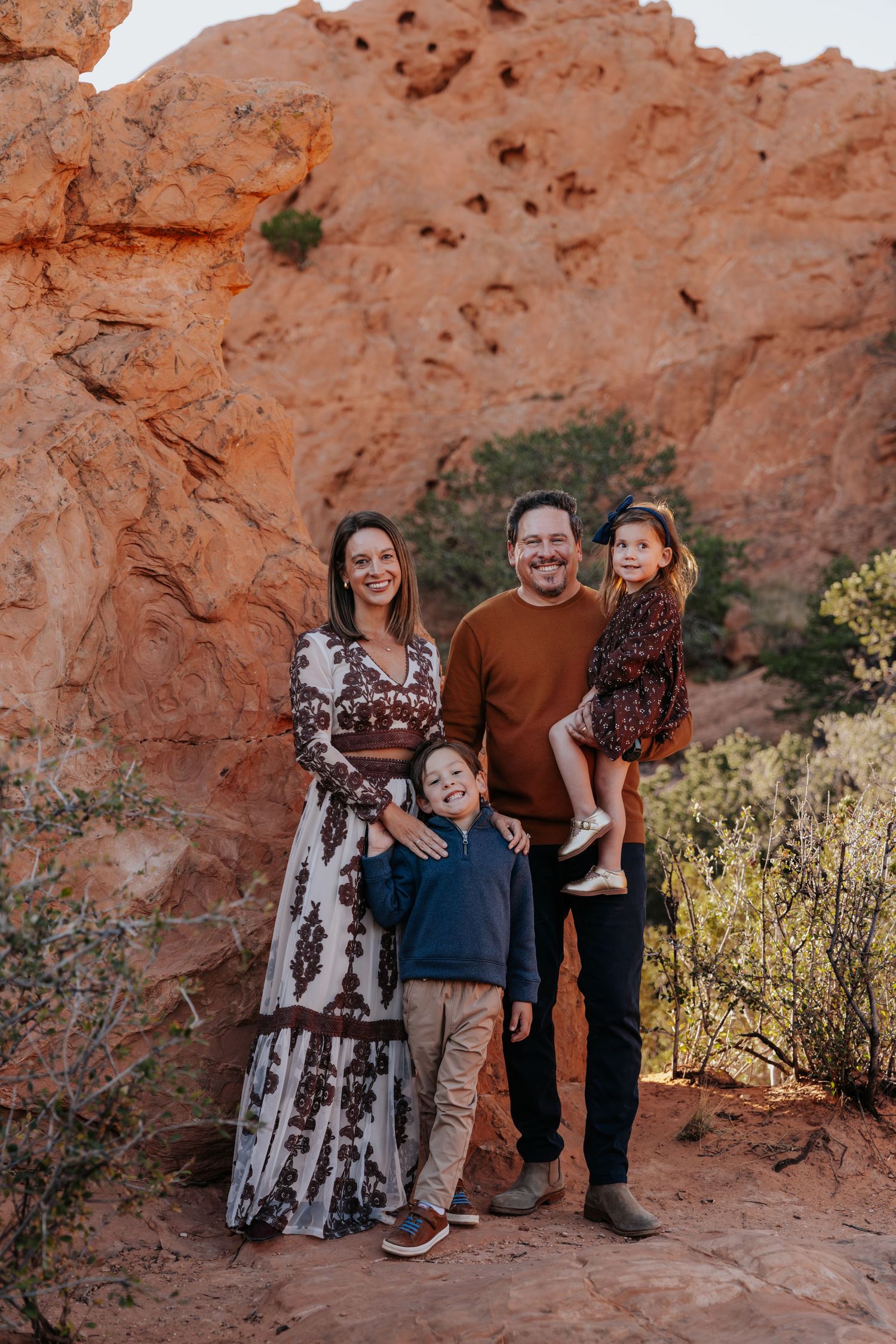 Happy family of four posing among red sandstone rock formations at Garden of the Gods Colorado.