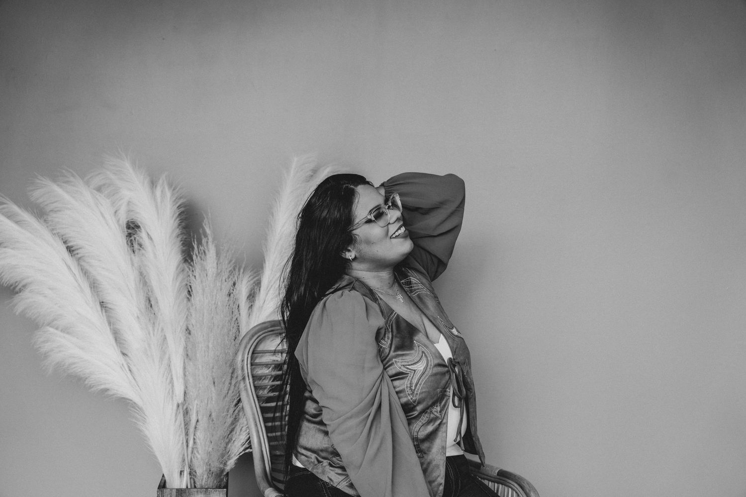 A black and white portrait of a woman laughing joyfully while seated beside decorative pampas grass.