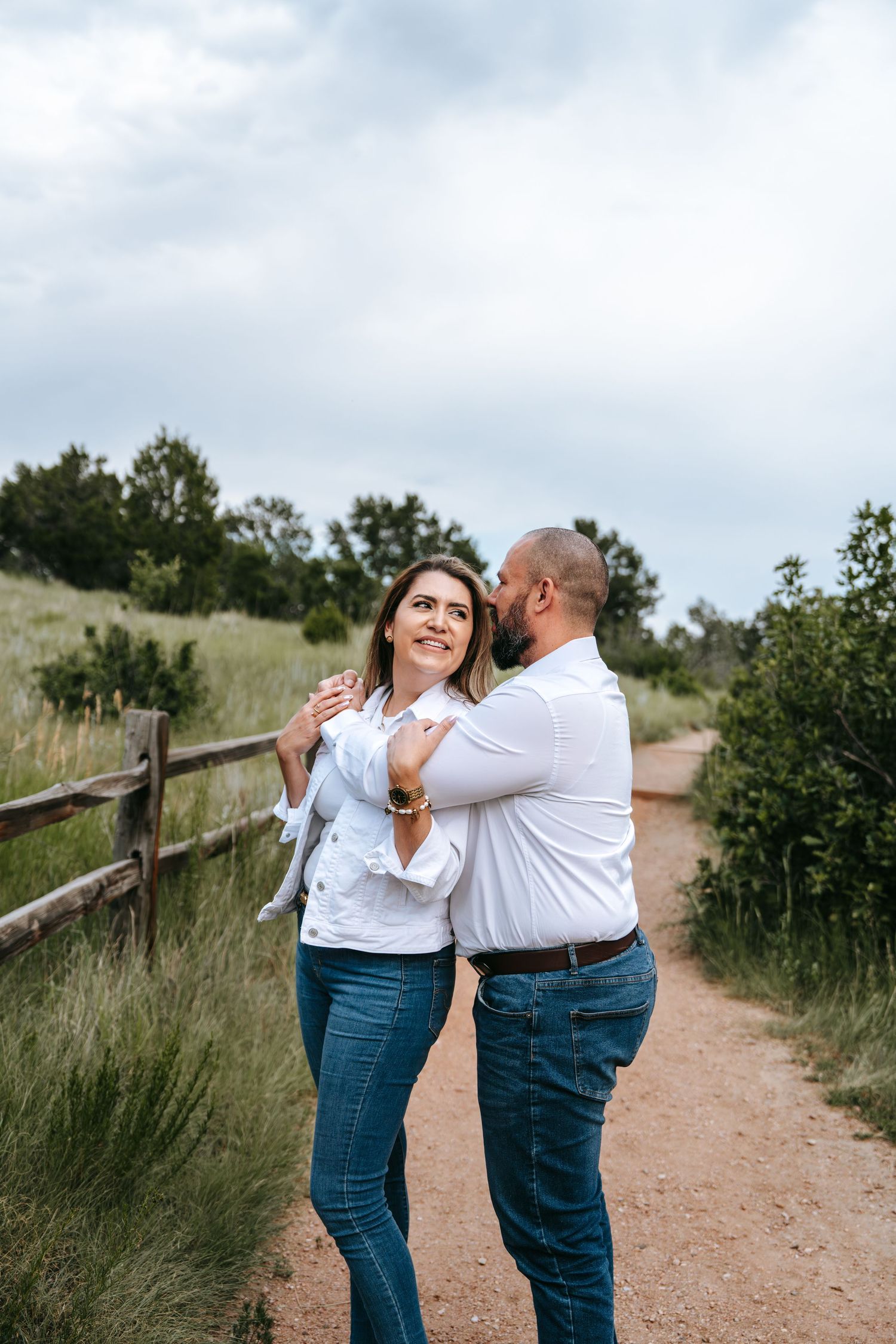 Couple embracing on dirt path, woman in white jacket smiling up at man in Colorado.