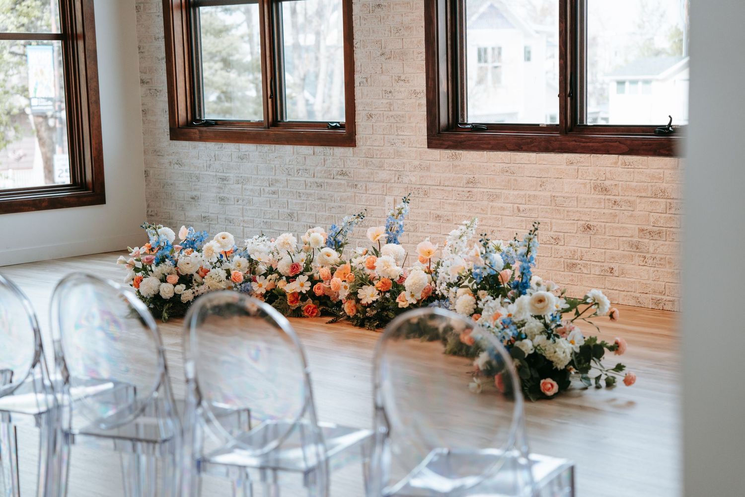 Colorful floral ceremony installation with pink, white, and blue blooms beside ghost chairs.