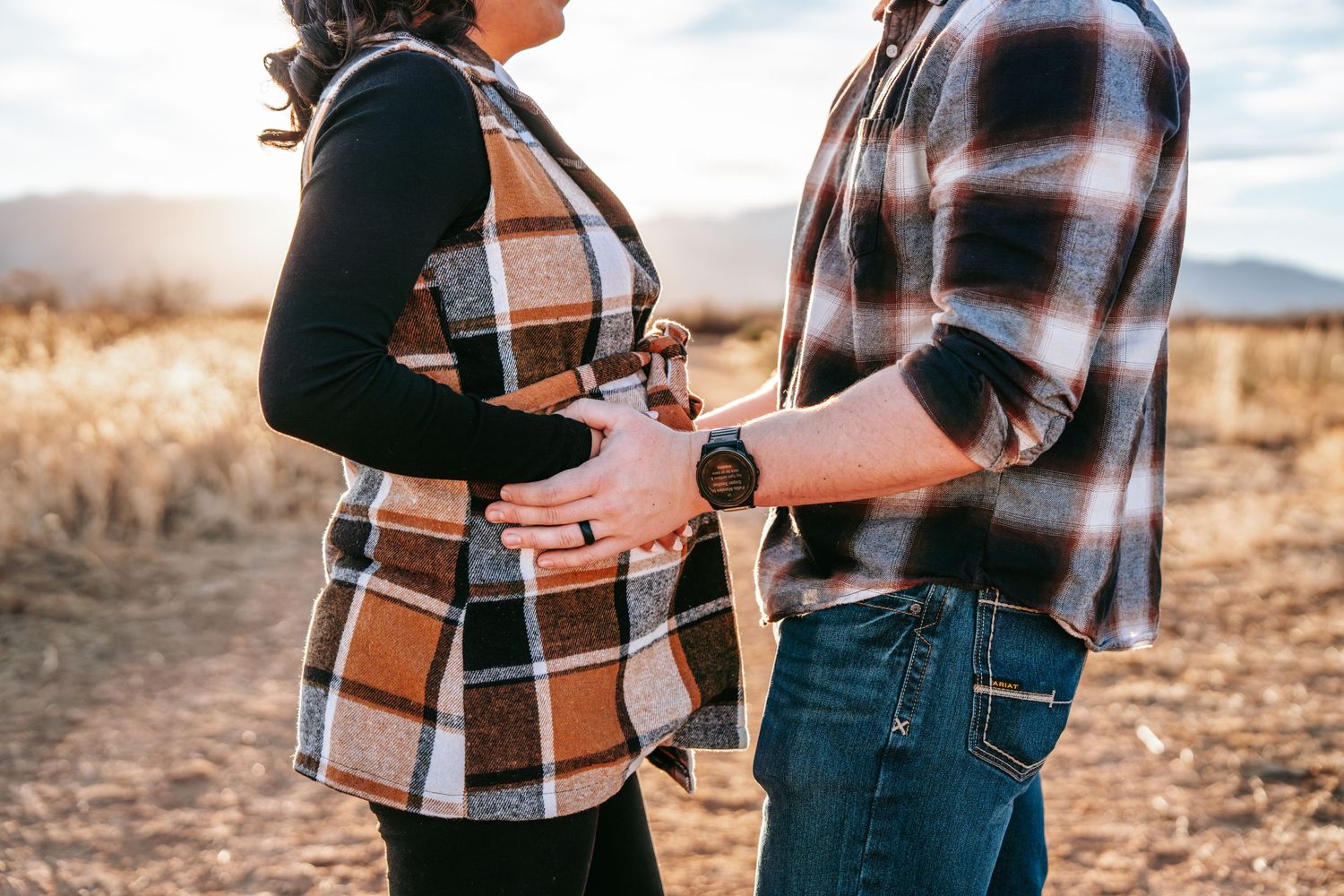 Close-up of pregnant woman's baby bump with partner's hand resting on it during outdoor maternity shoot.