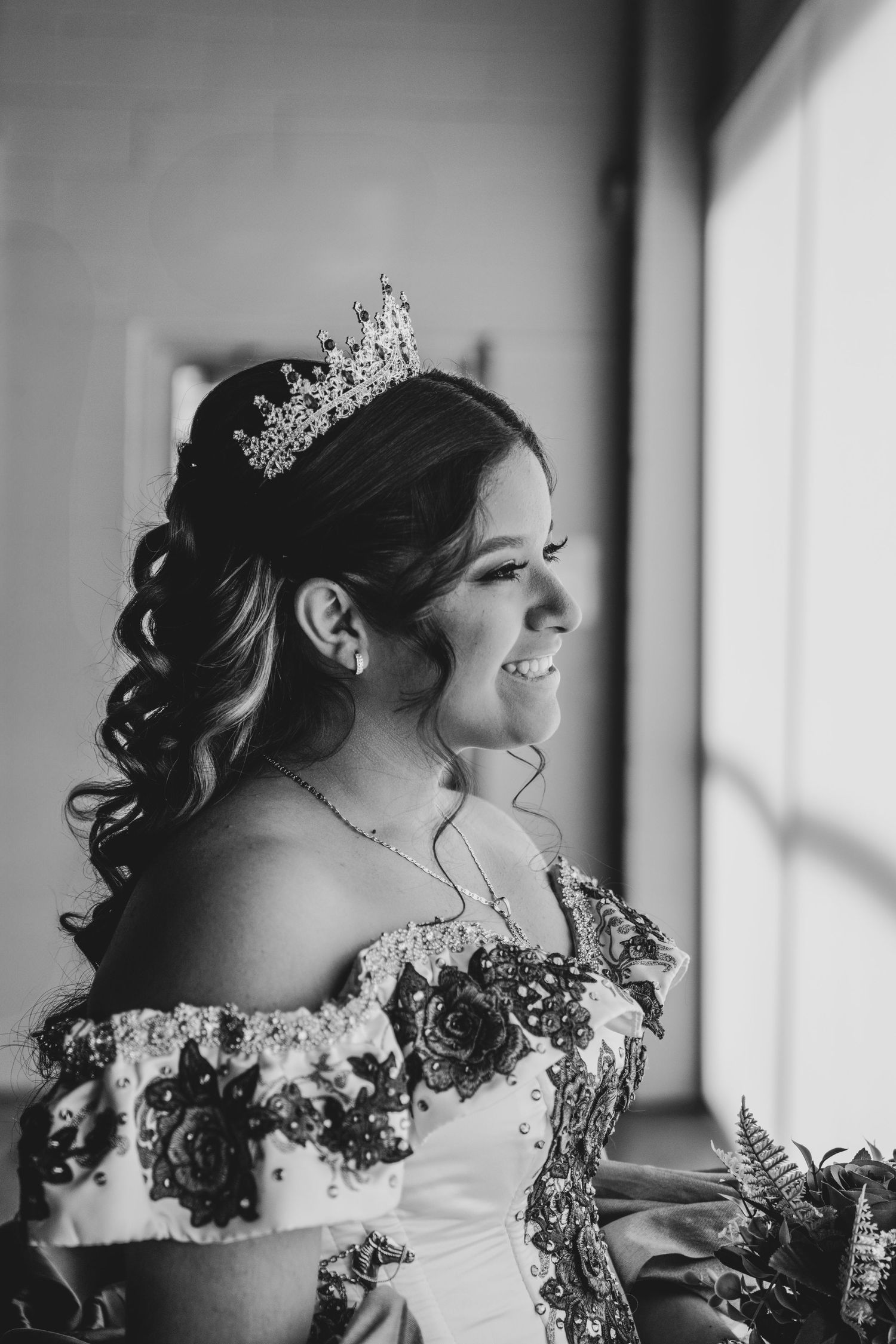 Black and white portrait of a smiling young woman in an off-shoulder gown wearing a tiara.
