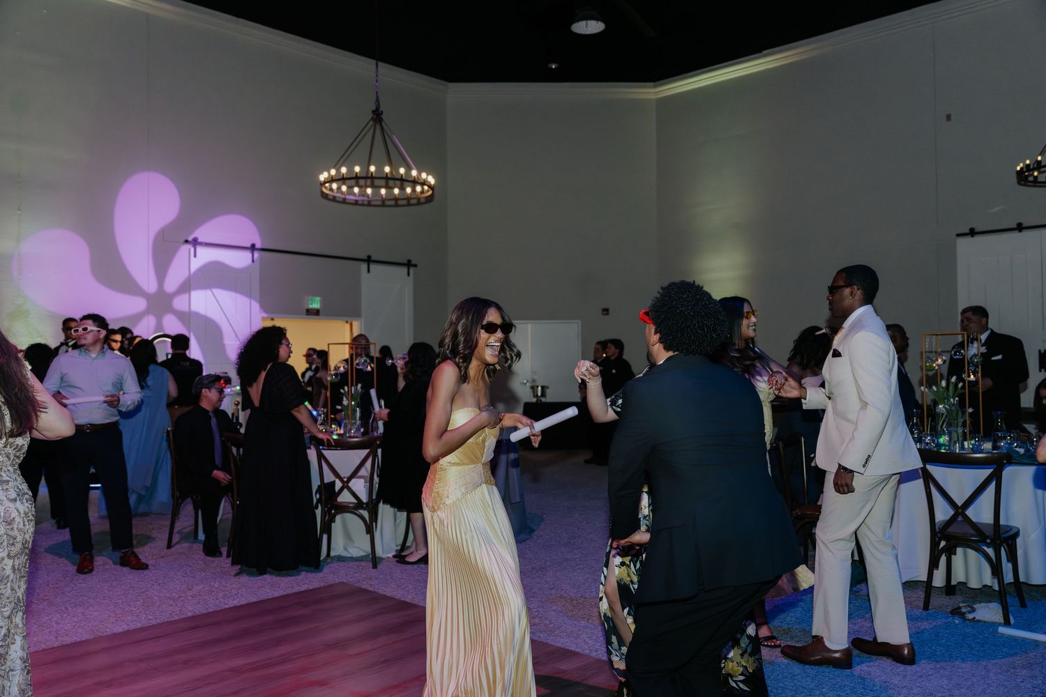 Elegant guests mingling at an upscale indoor event with purple lighting, chandelier, and stylish formal attire.