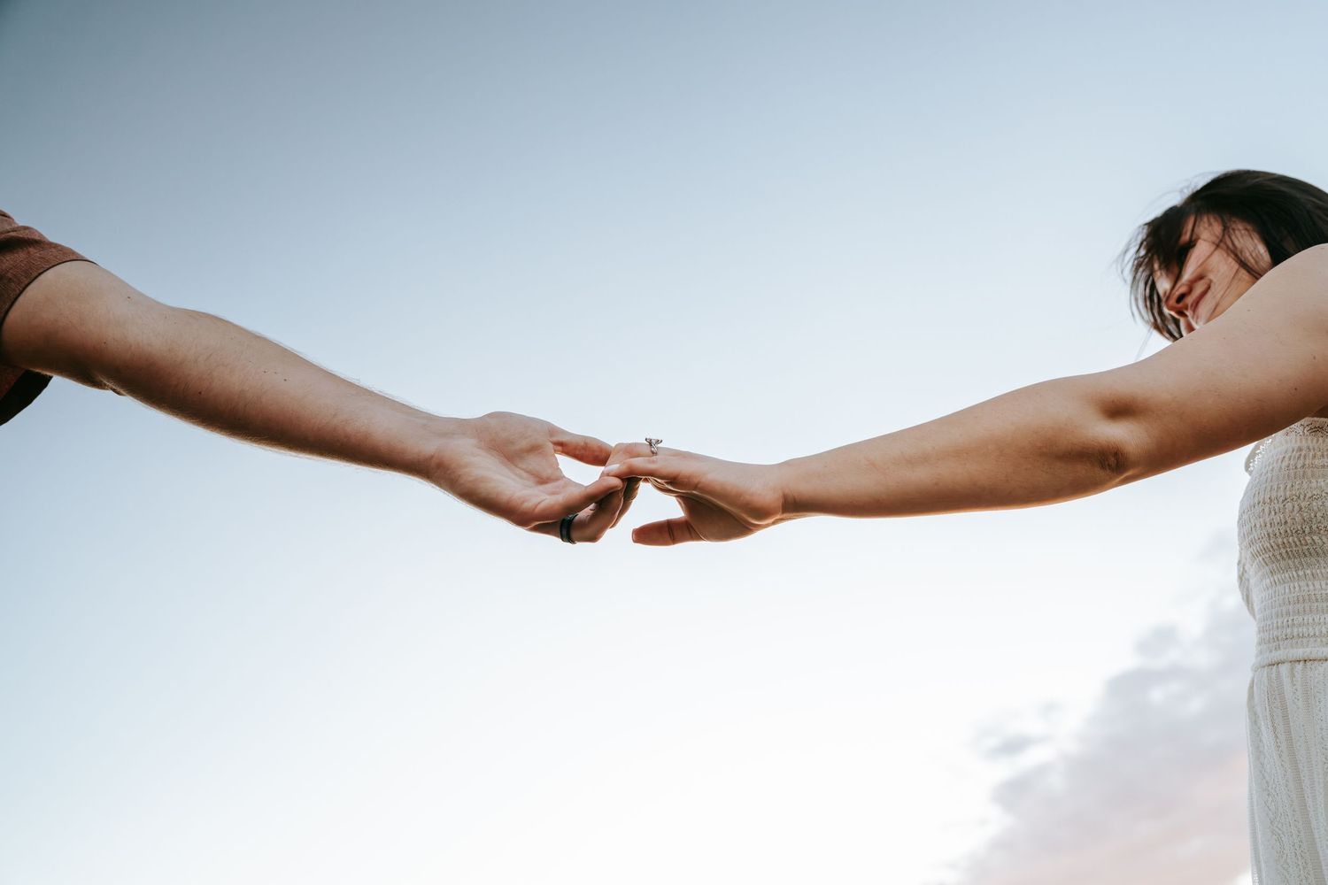 Two women gently touching fingertips outdoors against a soft blue sky, symbolizing connection and togetherness.