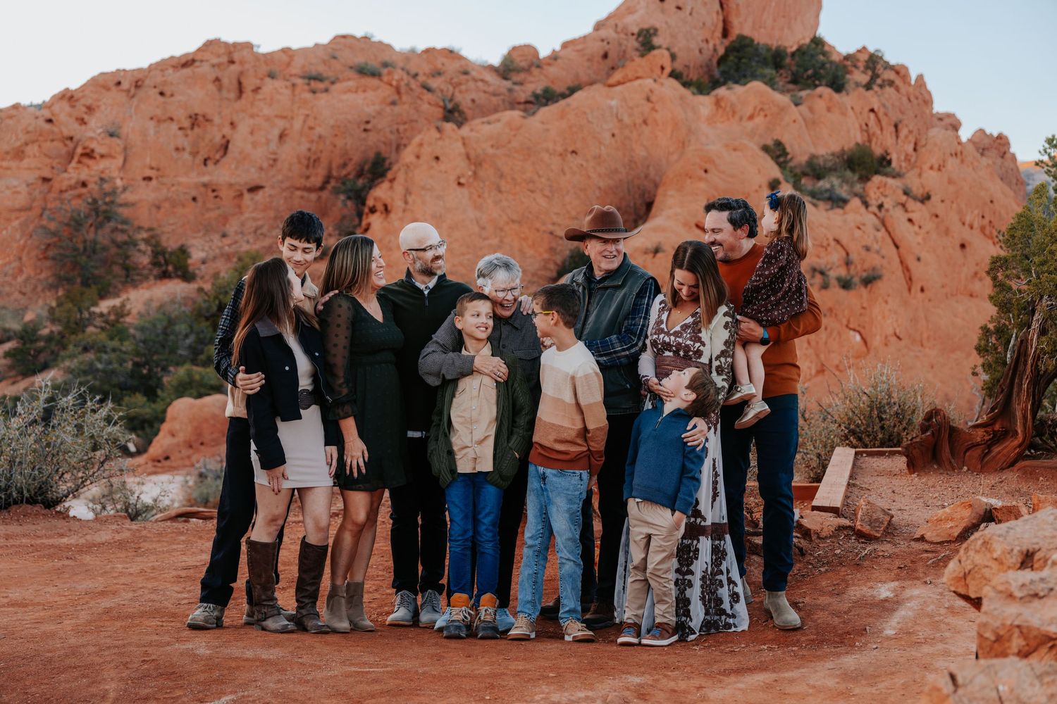Extended family laughing and gathered together on red desert ground with large red rock formations behind them.