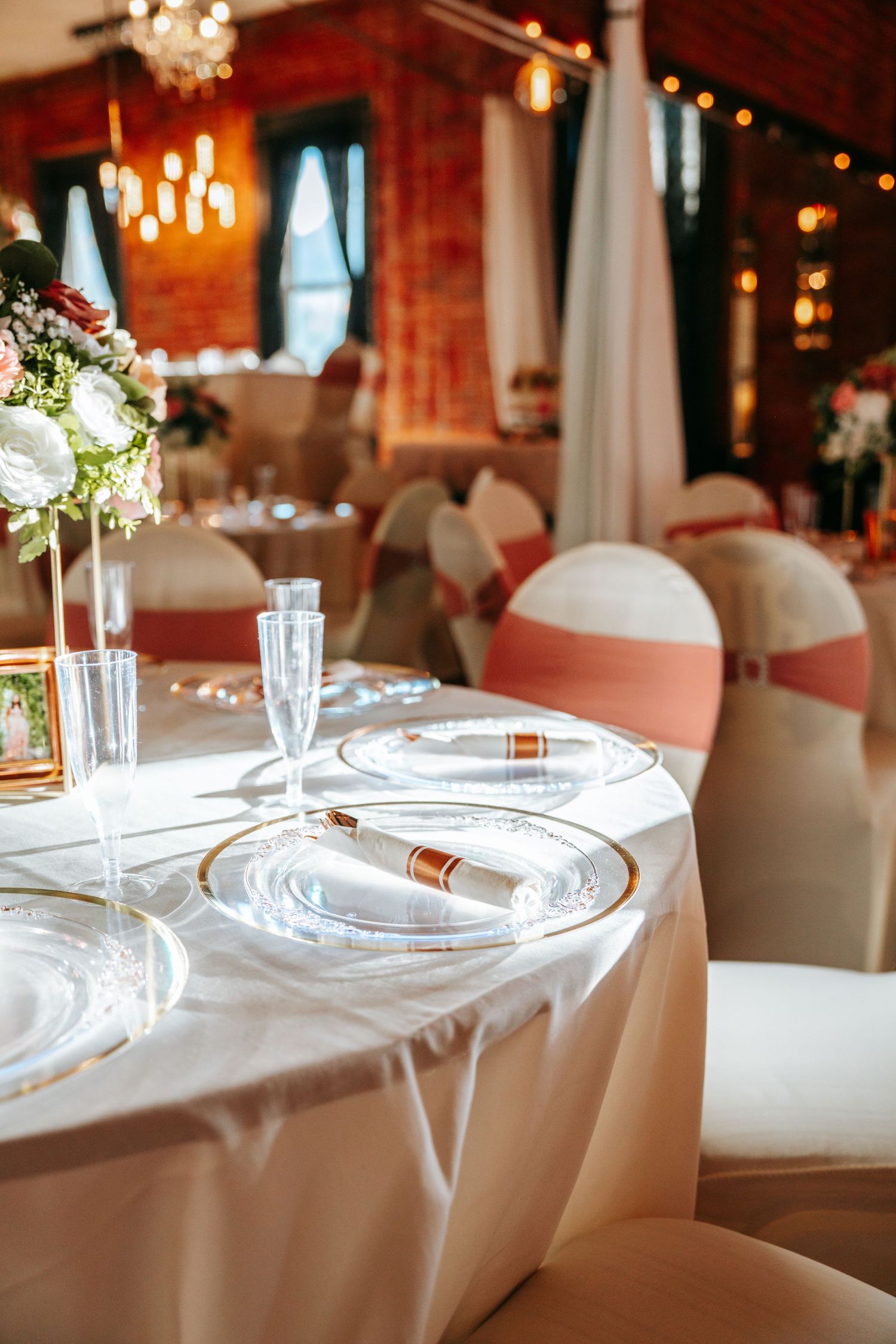 Formal wedding reception table setting with crystal glasses, white plates, and floral centerpieces.