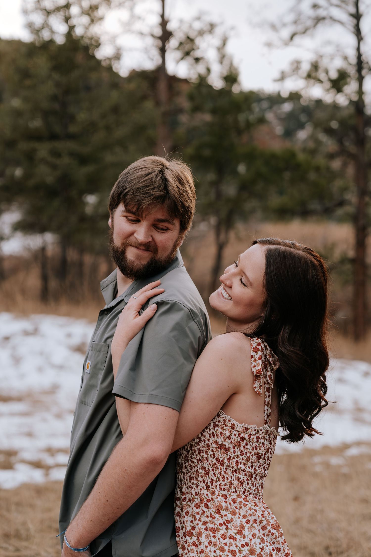 Couple embraces warmly in a snowy Colorado forest in a floral and gray outfit.