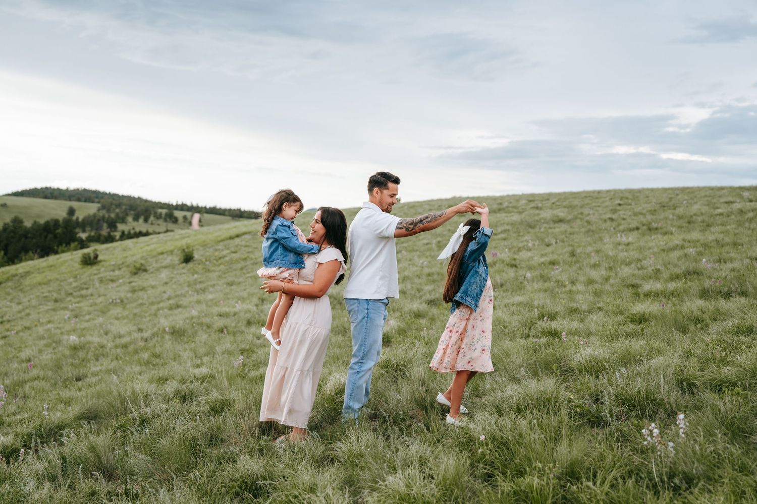 Family of four enjoying time together in lush green rolling hills under cloudy sky.