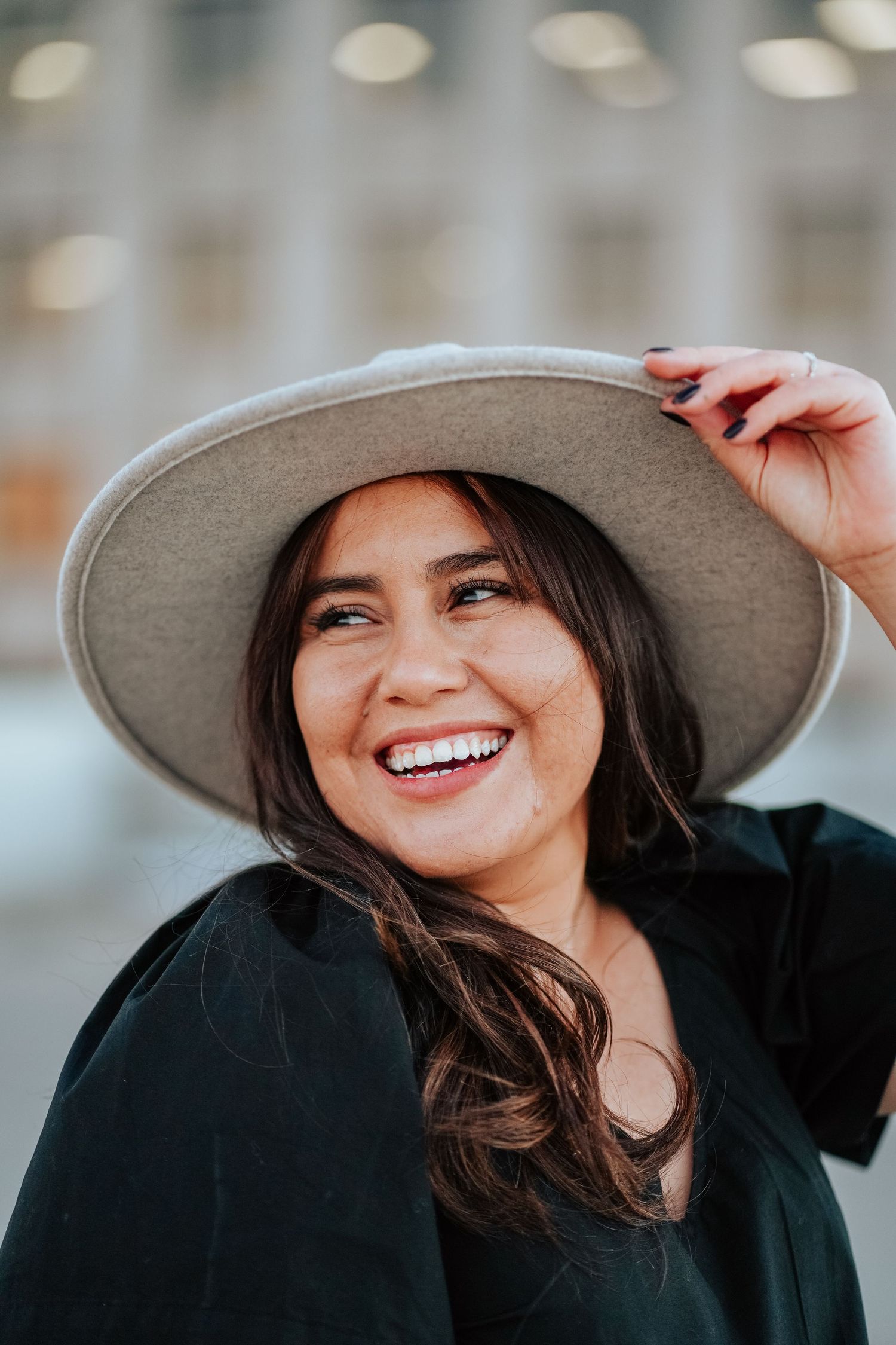 Happy young woman in a gray wide-brim hat laughing outdoors.