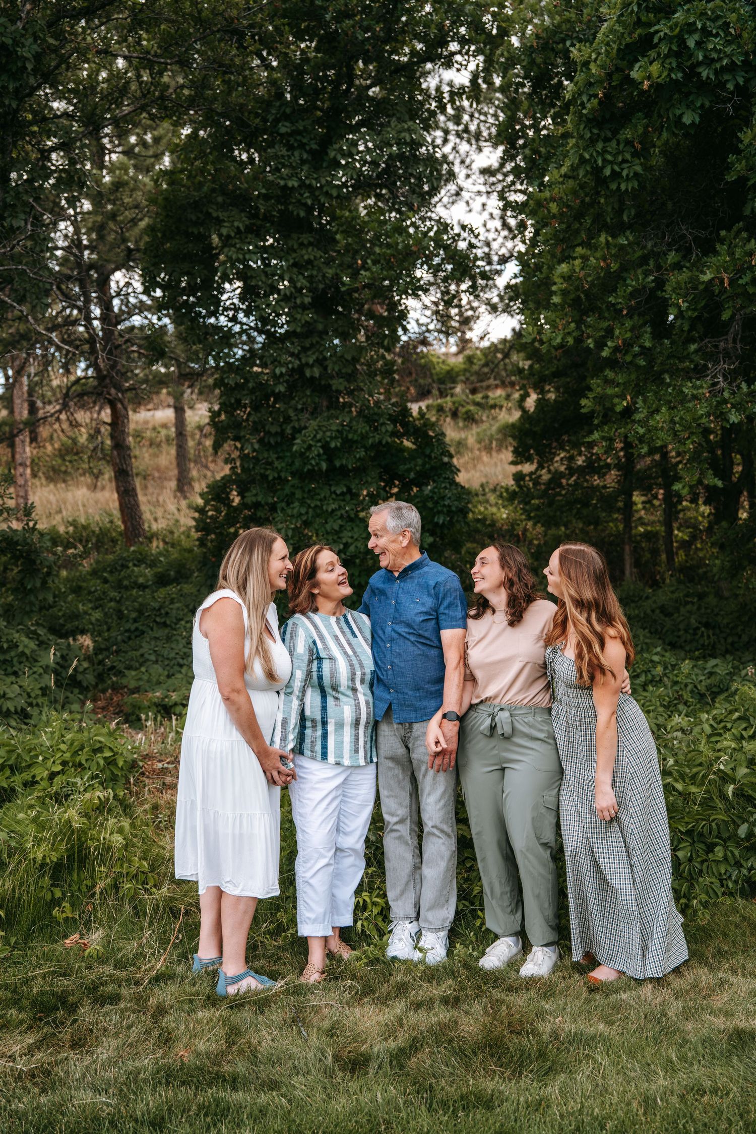 A happy family of five poses together outdoors on a green lawn surrounded by lush trees.